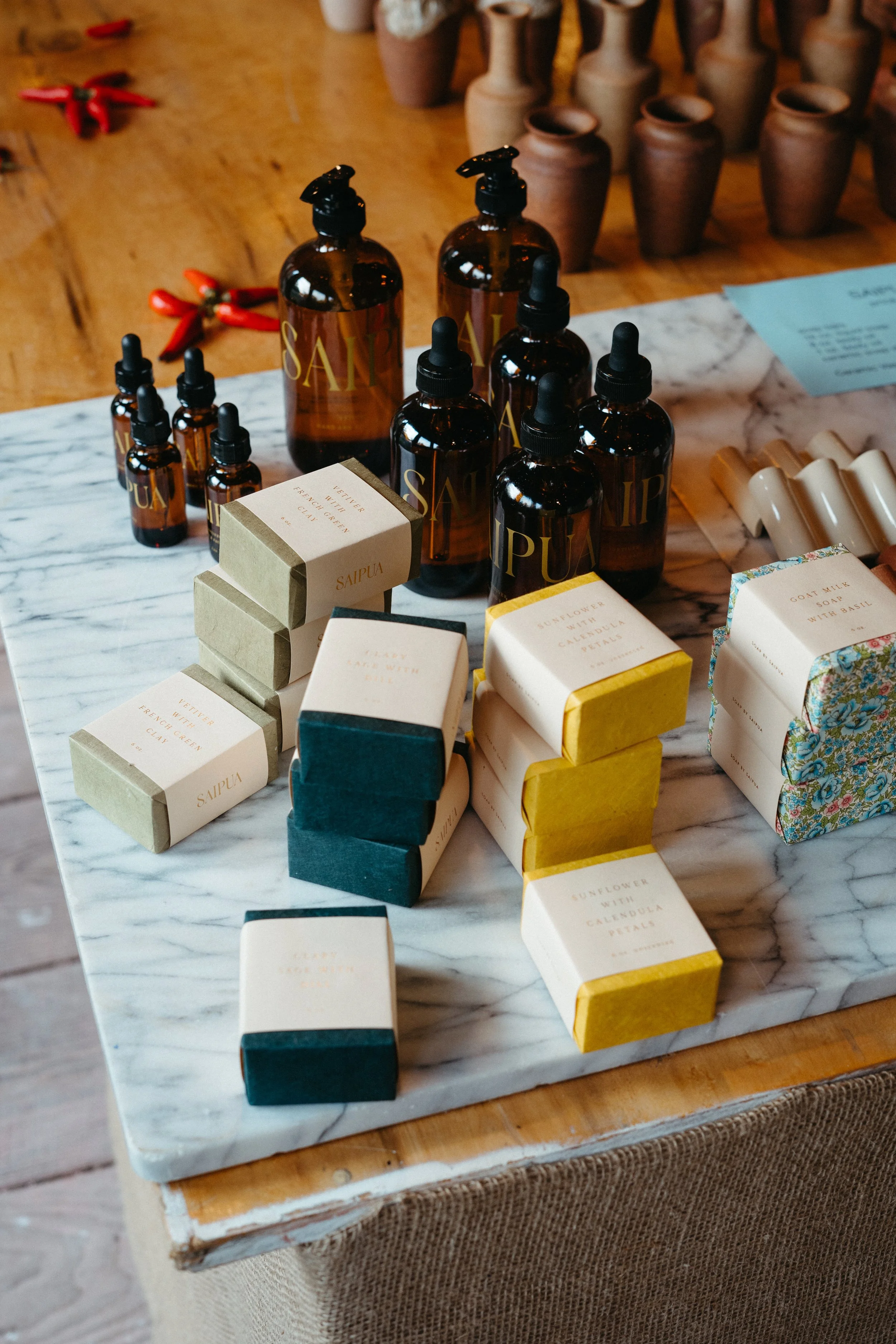 A display of various soap and skincare products on a marble countertop, including amber bottles with dropper caps, soap bars in paper packaging, and other toiletry items.