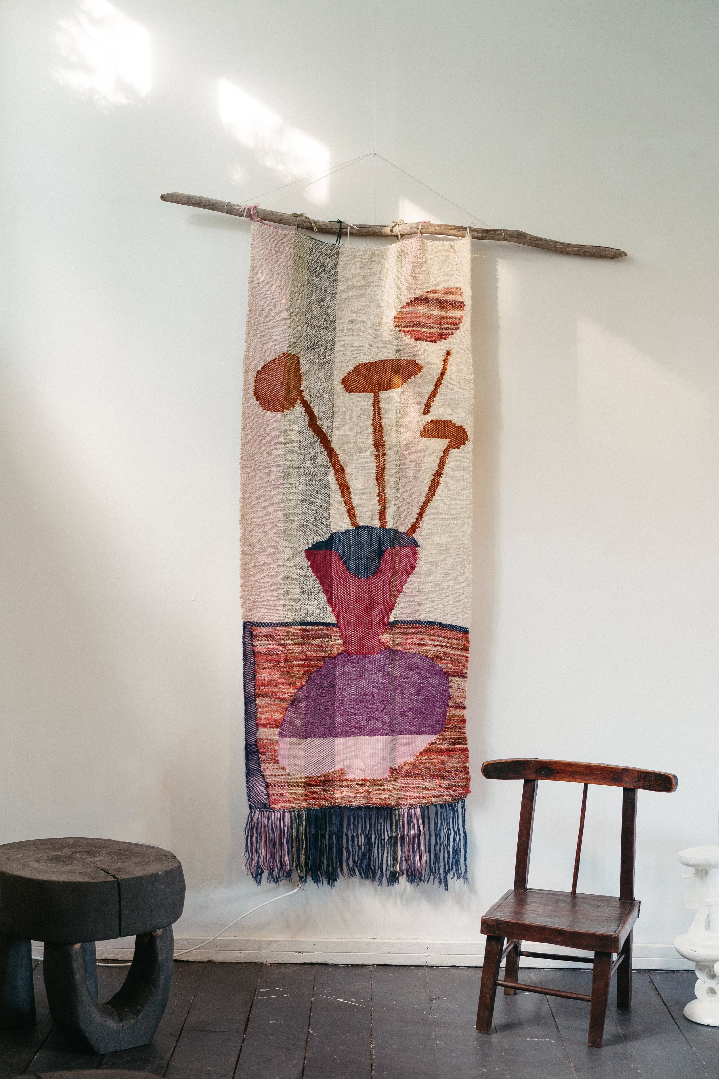 A decorative wall hanging with an abstract floral design, displayed on a wall above a wooden chair and other furniture.