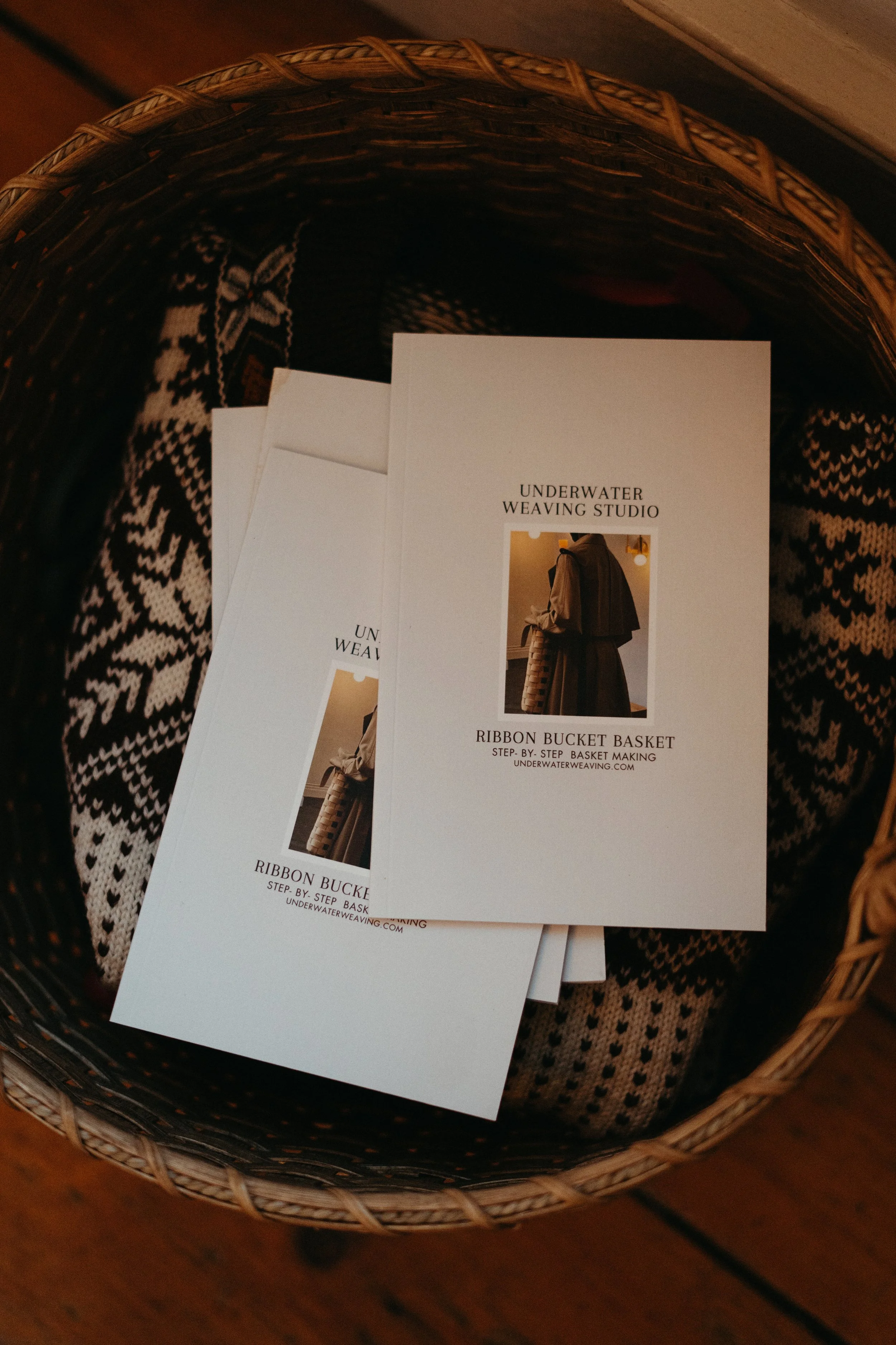 Brochure or flyer for underground weaving studio featuring a woman holding a ribbon bucket basket, placed inside a woven basket atop a patterned textile.