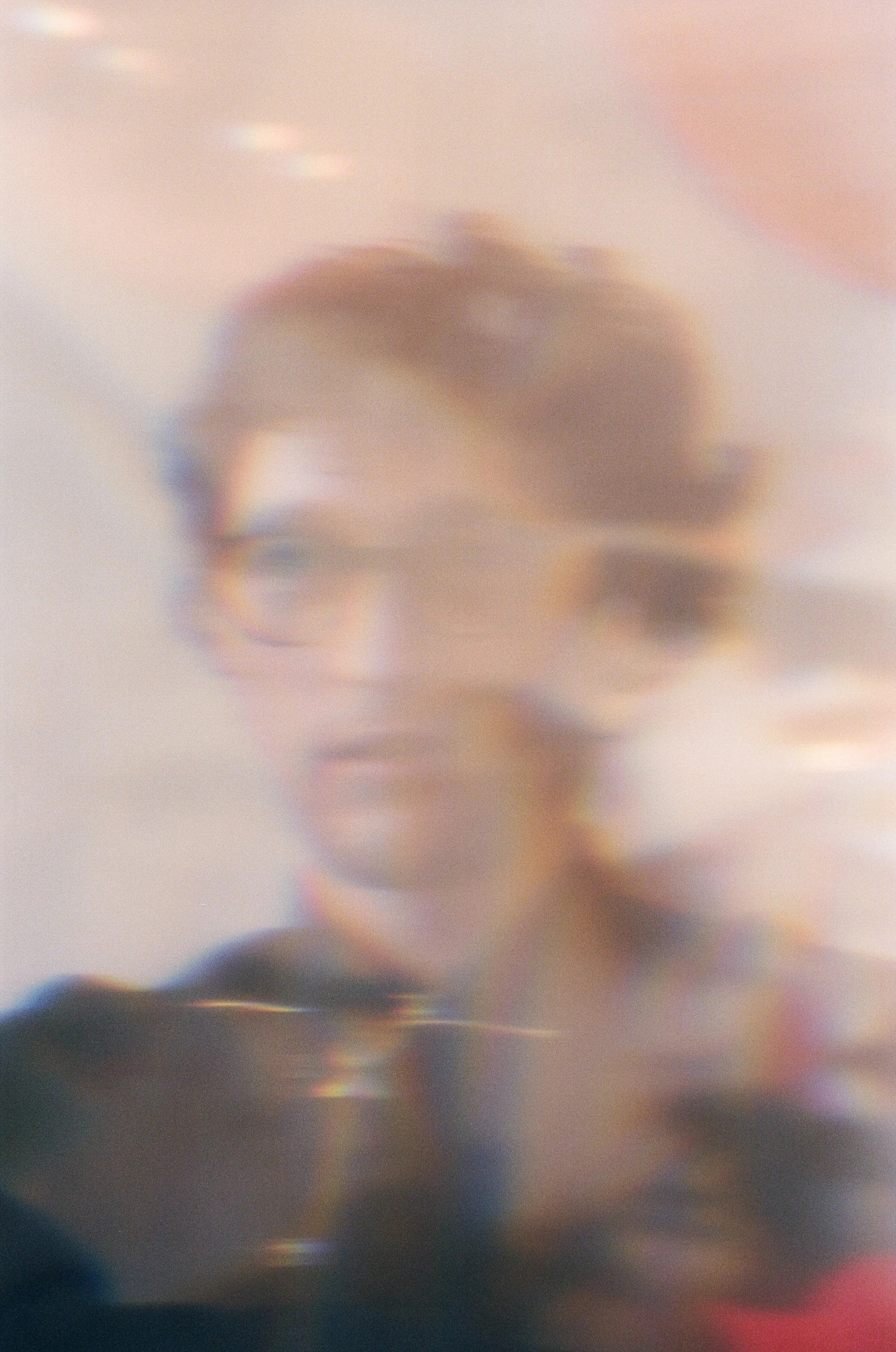 Blurry photo of a man wearing glasses, with a soft, pastel-colored background.