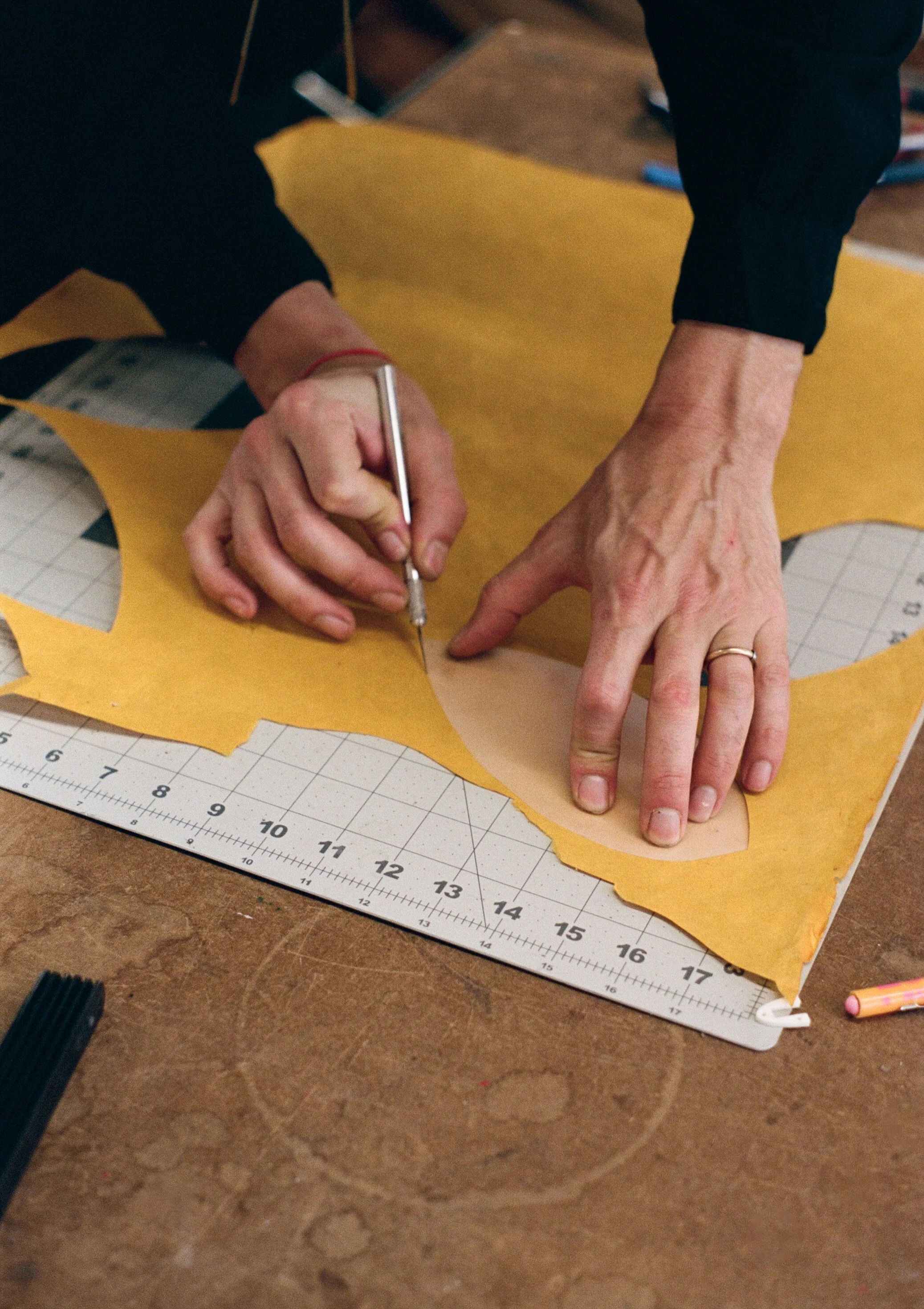 A person sewing leather using a cutting pattern on a worktable.