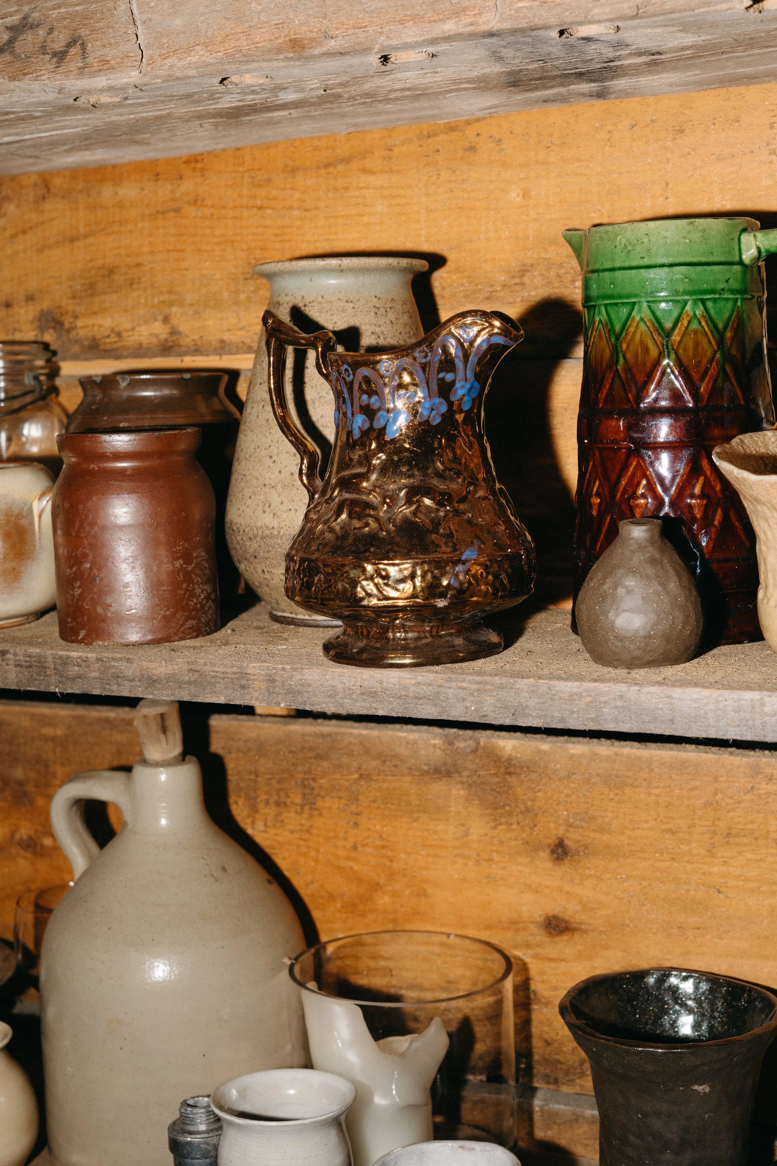 Collection of antique pottery and ceramic vases arranged on wooden shelves with rustic background.