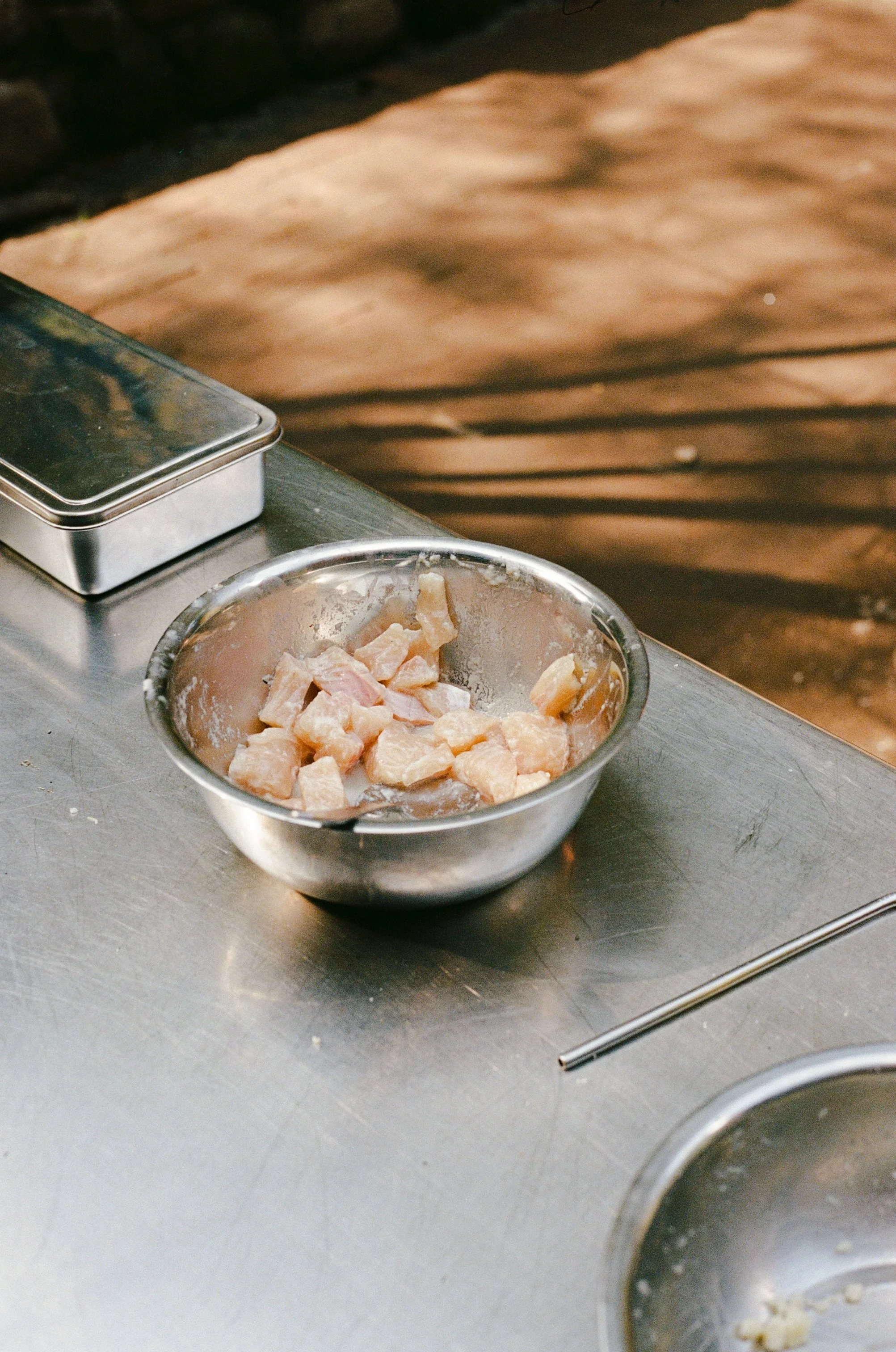A metal bowl filled with raw, cubed chicken pieces on a stainless steel countertop.