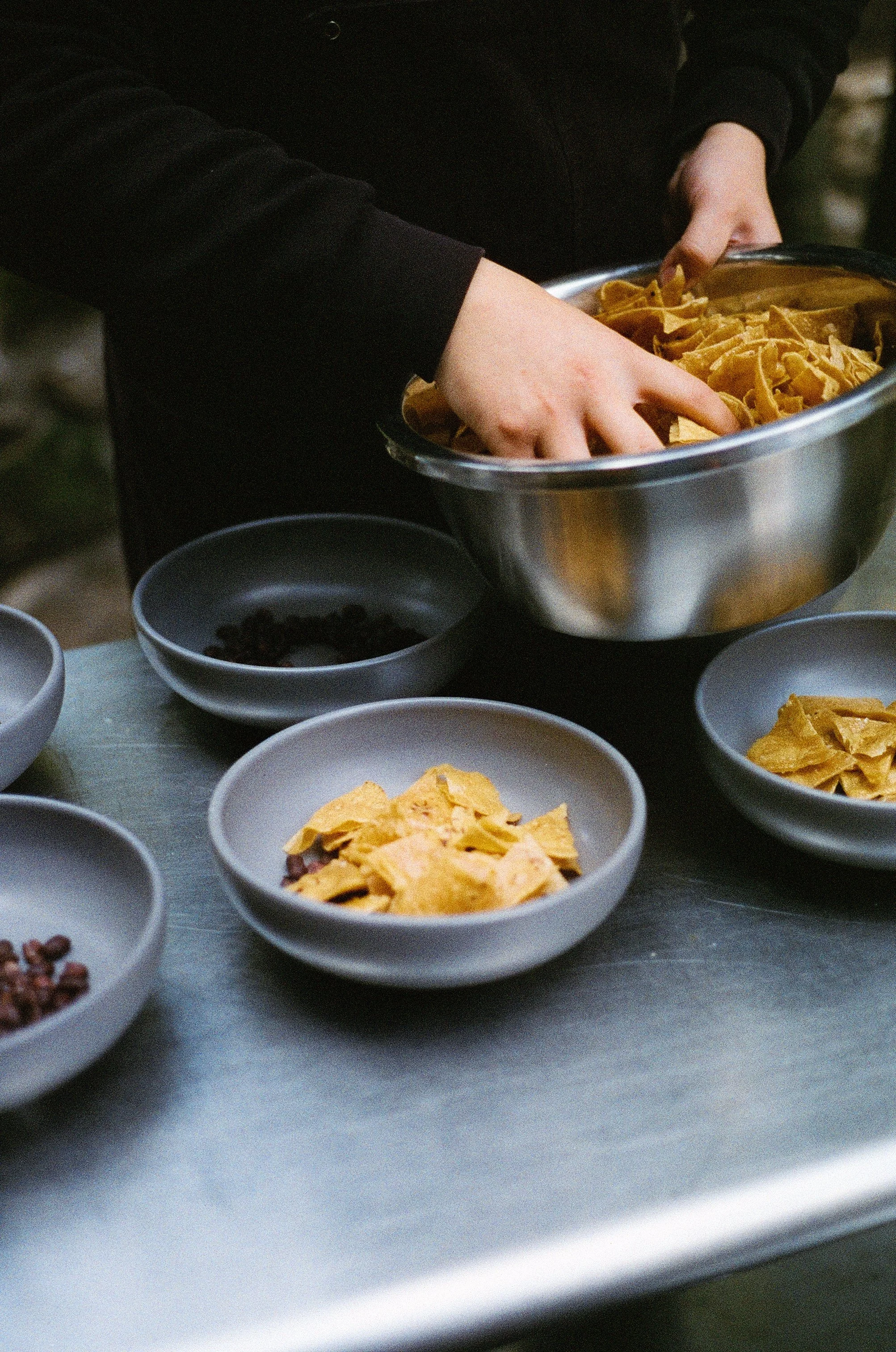 Person serving tortilla chips into bowls at a table.