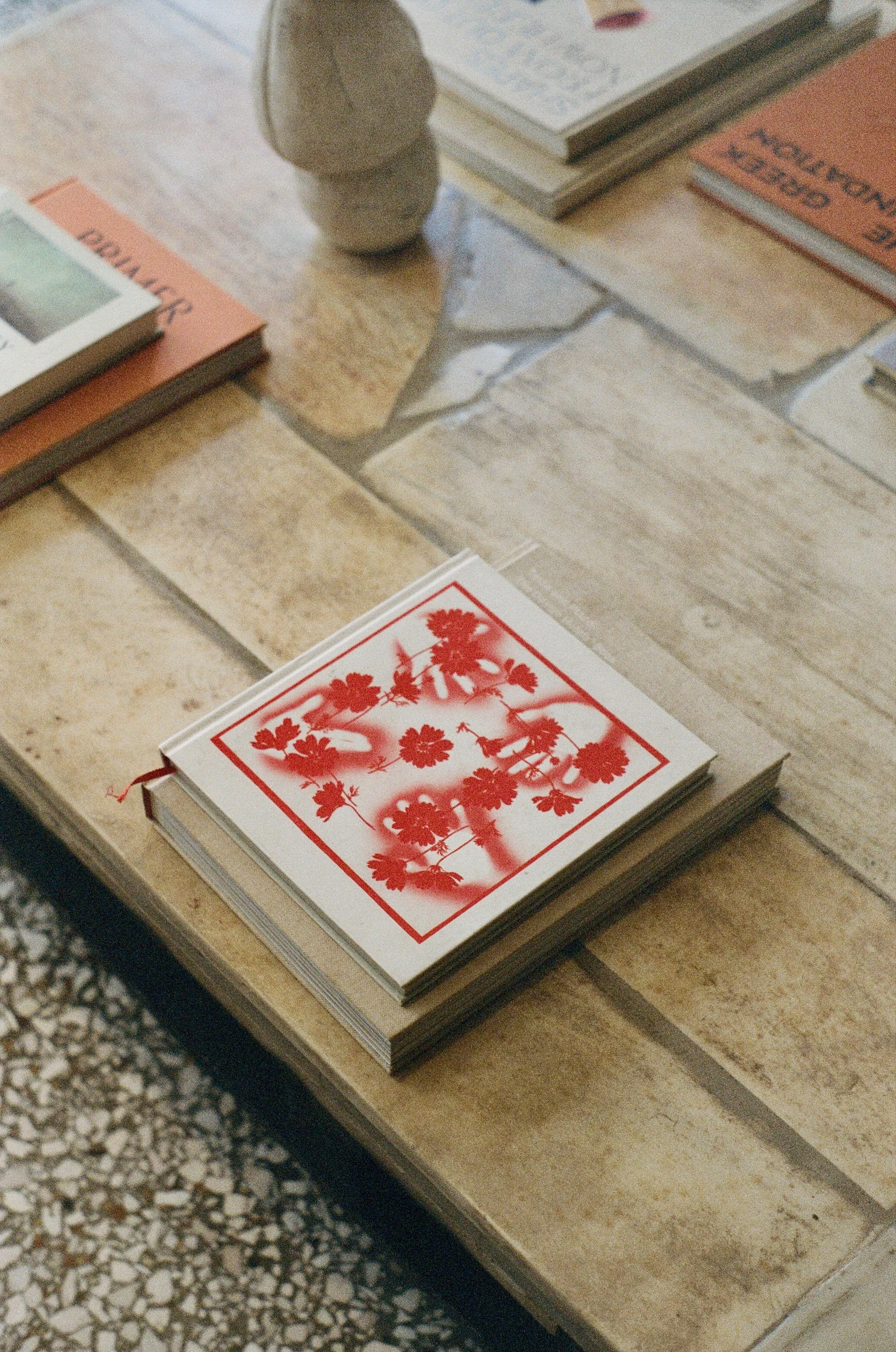 A wooden table with several books and a small decorative vase on top, including a book with a red floral design on the cover.