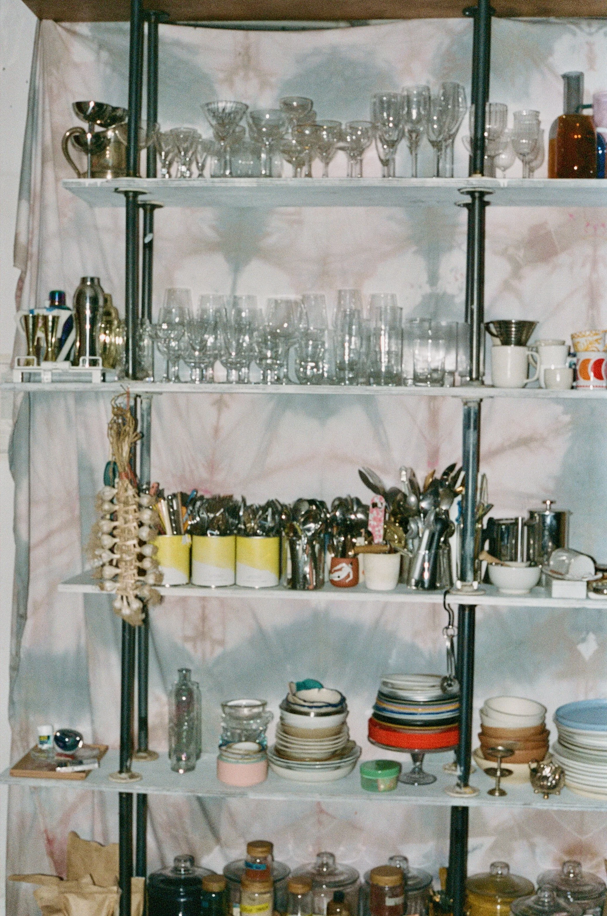 A shelving unit filled with various glassware, kitchen utensils, mugs, plates, and jars.