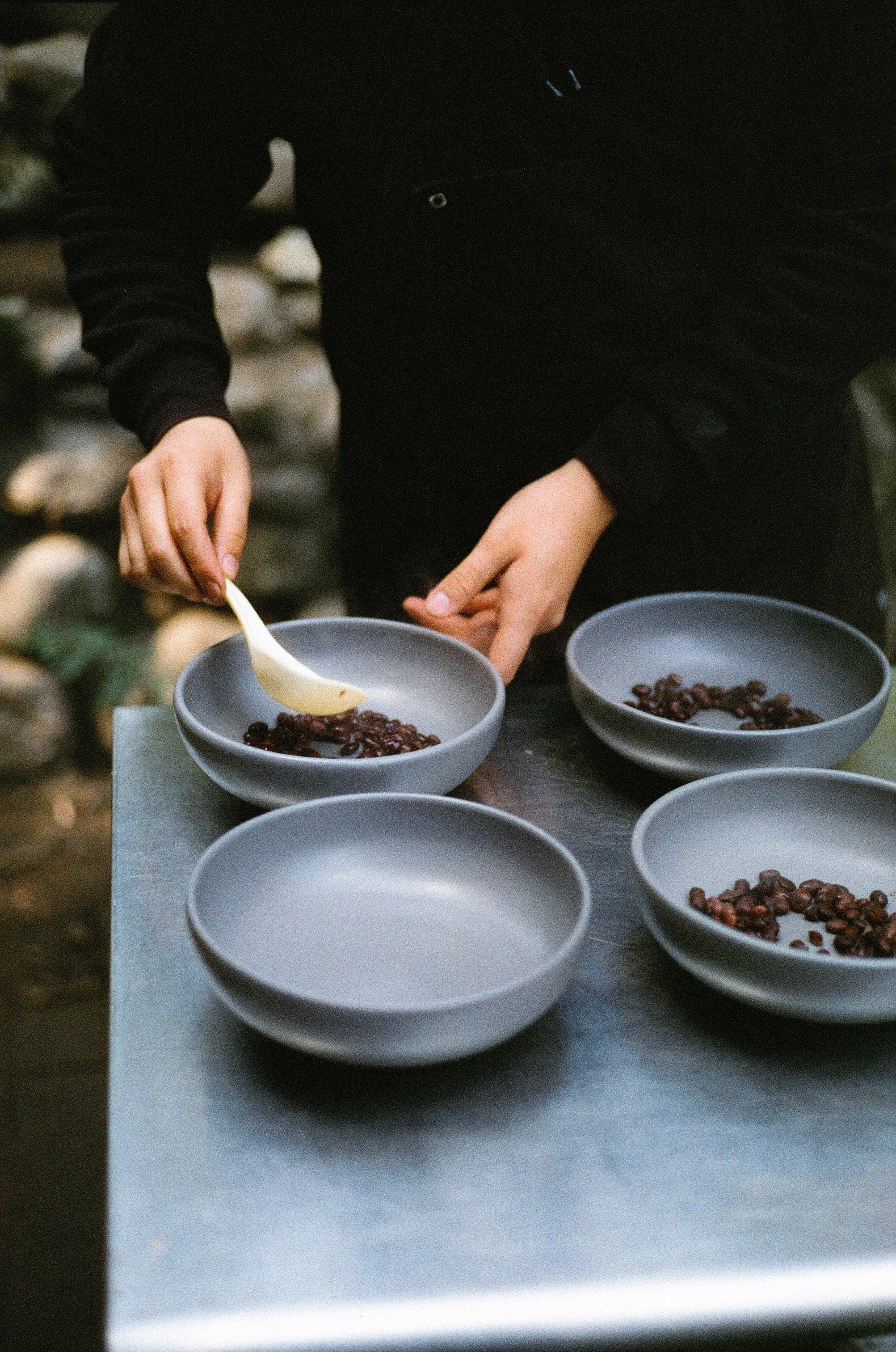 Person scooping dried berries into grey bowls on a metal table outdoors.