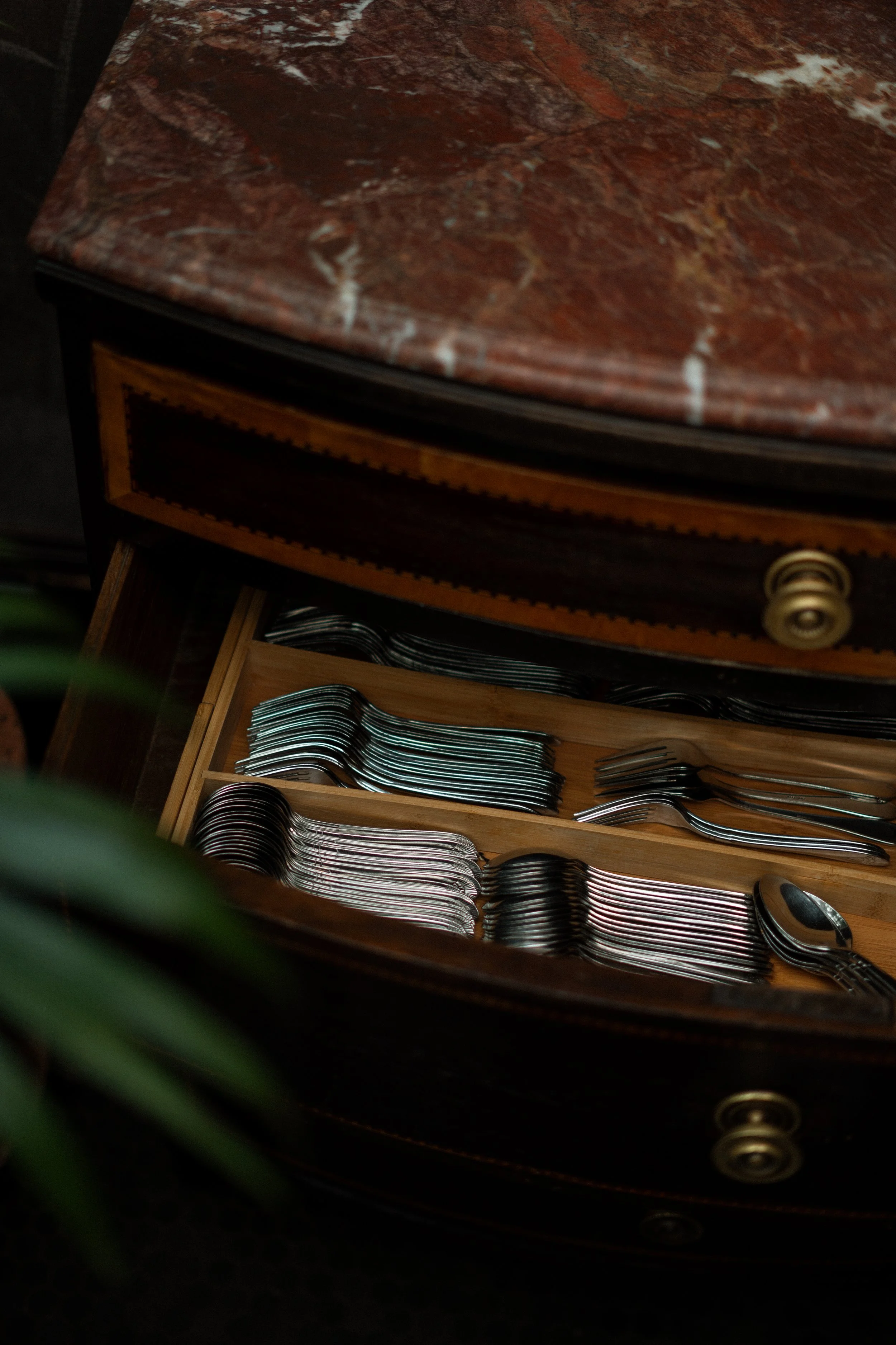 Open drawer of a vintage wooden table with neatly arranged forks and spoons.