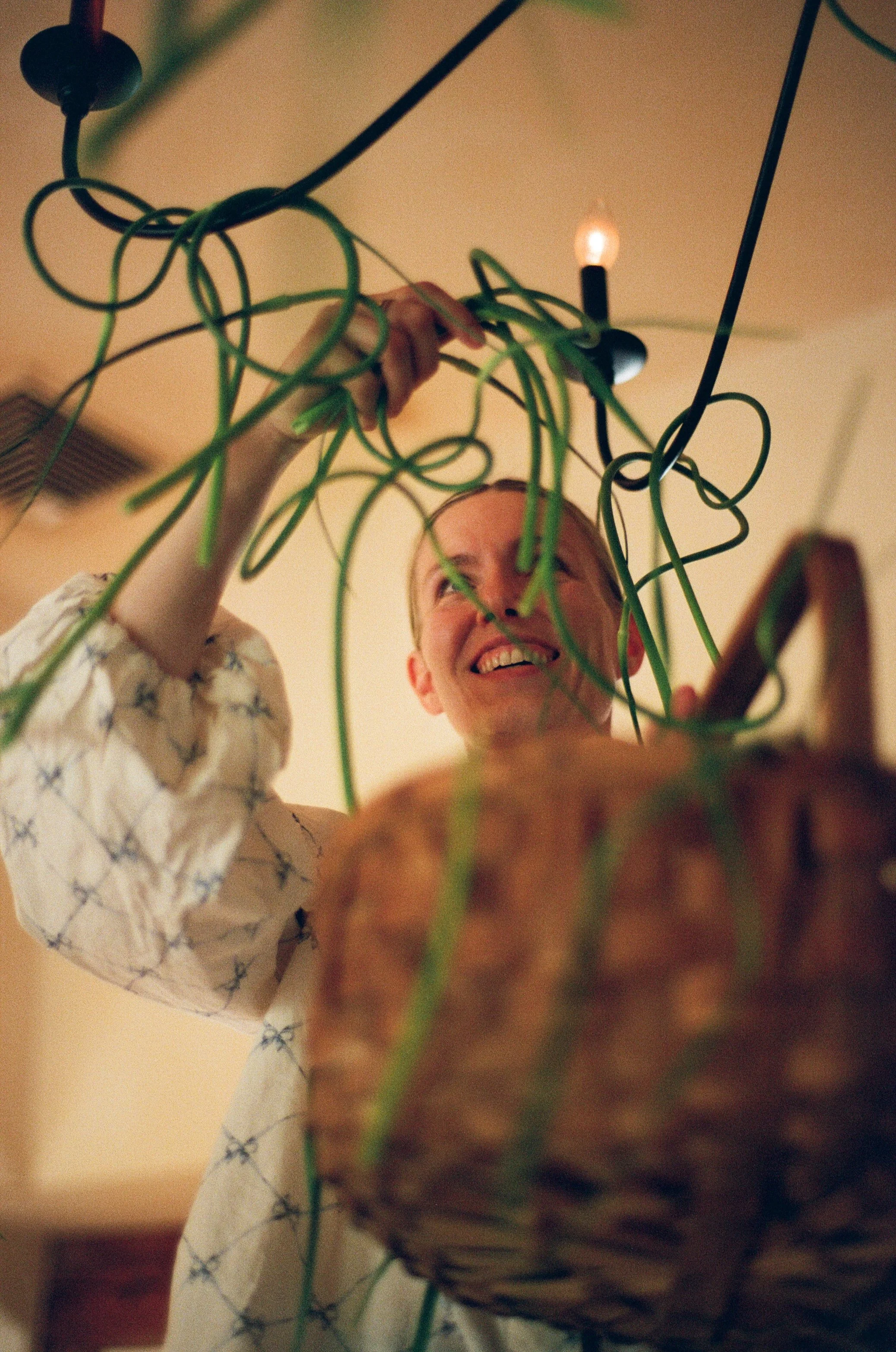 A man smiling as he enjoys hanging light bulbs with green electrical cords from the ceiling, with a basket in the foreground.
