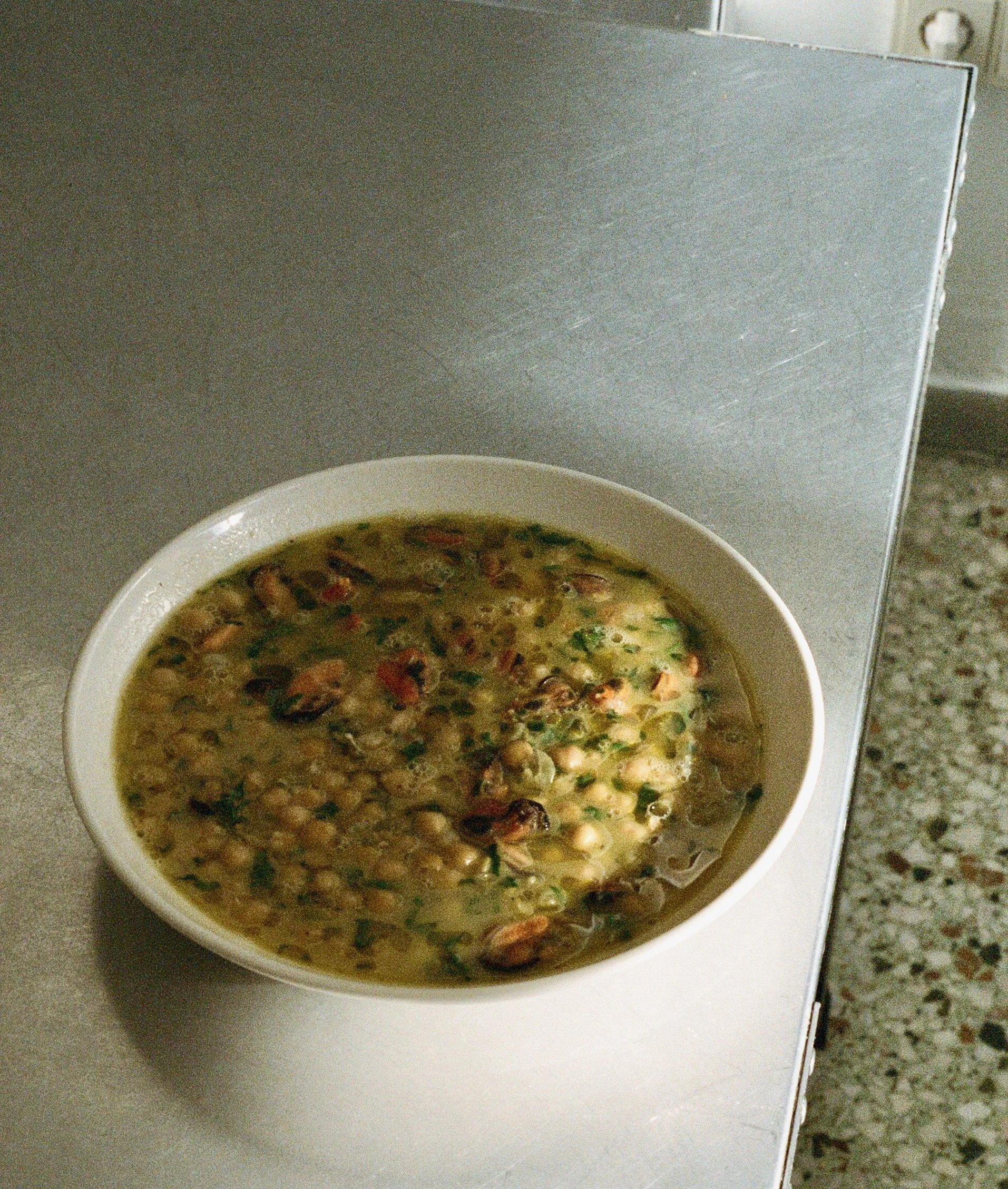 A bowl of soup with beans, herbs, and possibly vegetables on a white countertop.