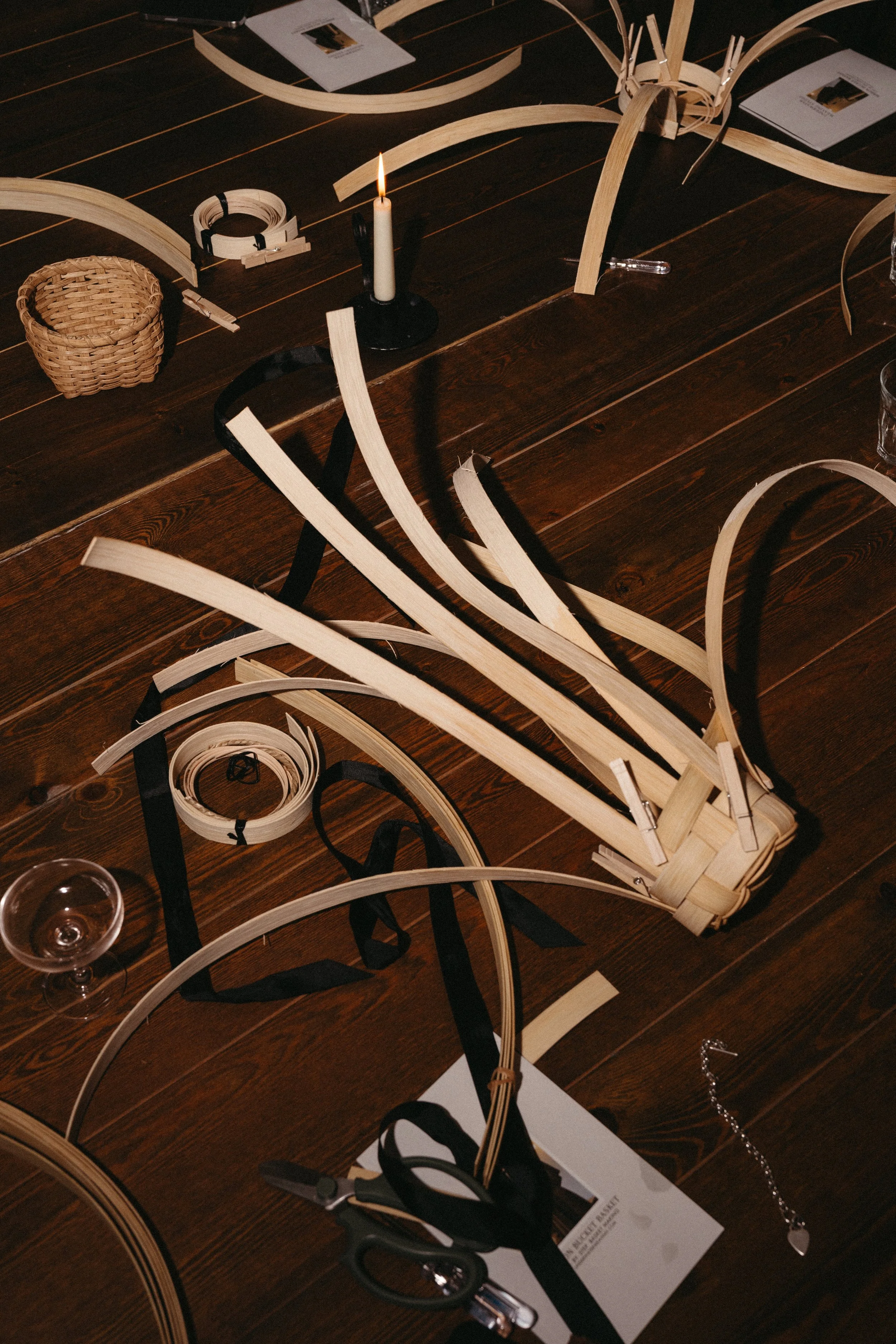Unfinished wooden art or craft project on a dark wooden table, with various tools, a candle, ribbon, and paper scattered around.