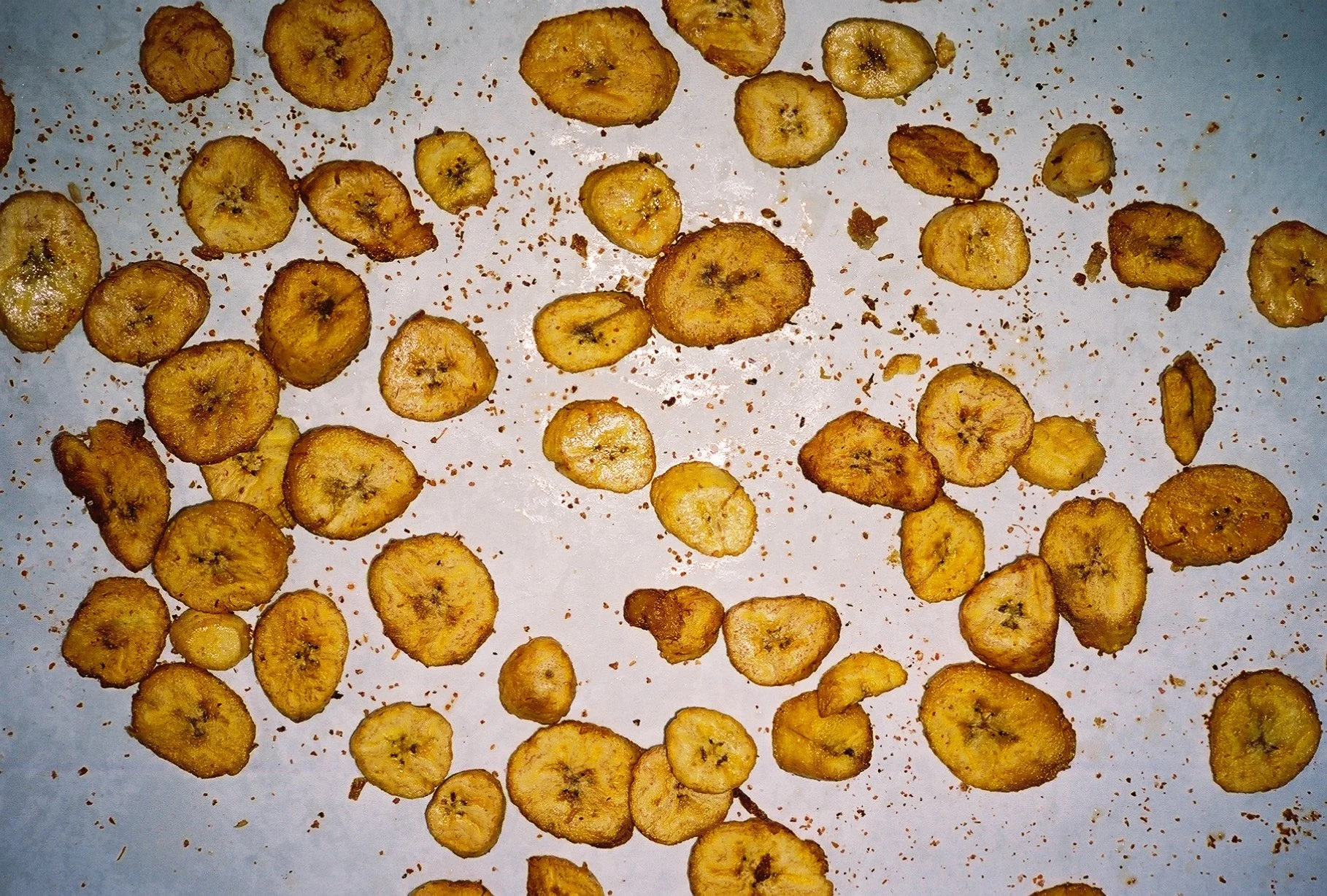 Freshly sliced banana chips scattered on a white surface.