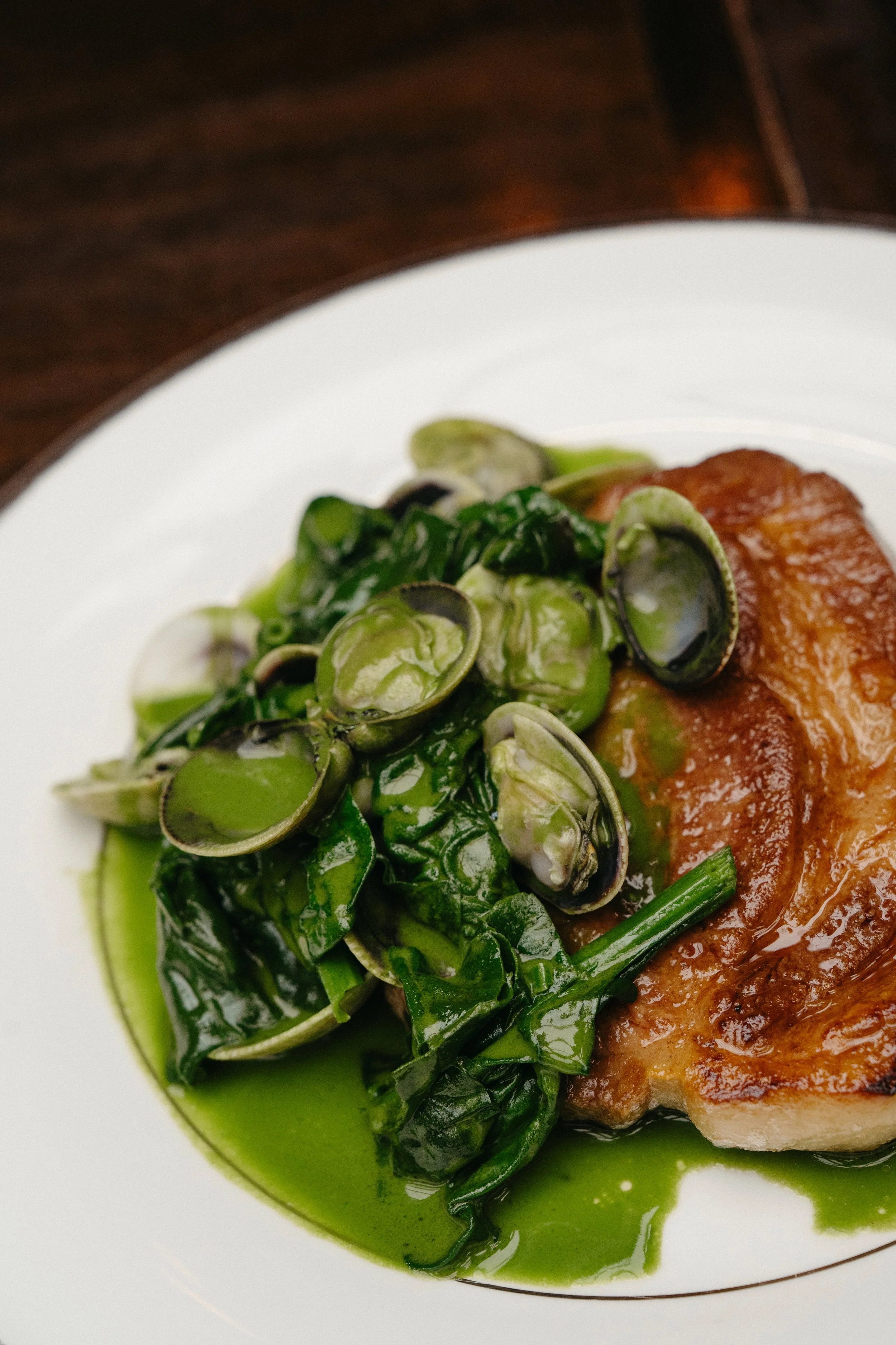 Plate with cooked meat, green vegetables, and clams with green sauce.
