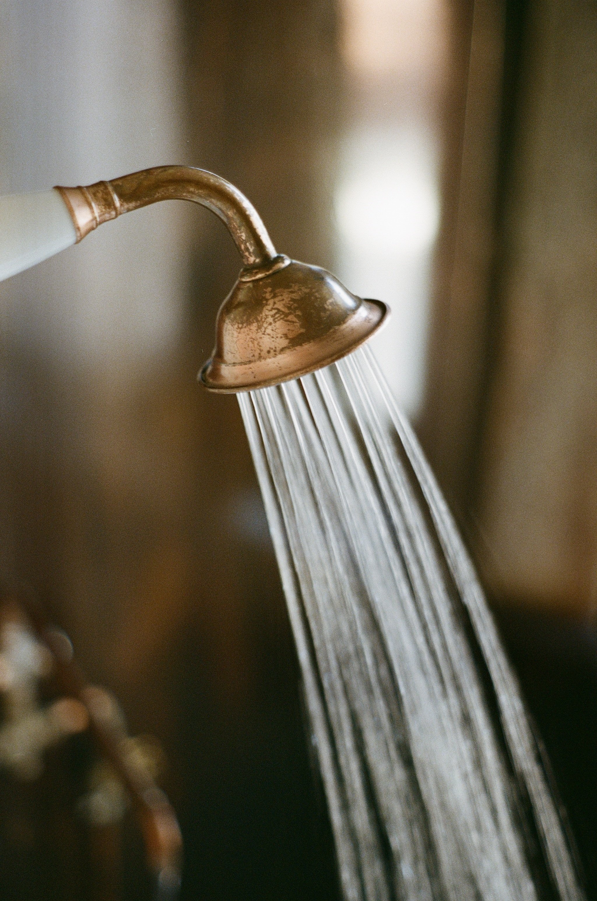 Close-up of a vintage copper outdoor shower head with water flowing.