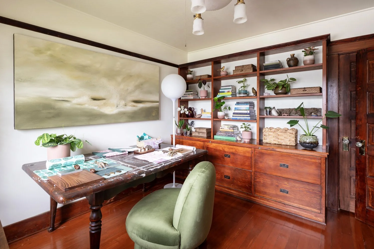 Photo by: Steven Dewall
A large-scale hazy landscape painting by Peter Burega hangs over the work area, creating a calming presence within the room. The green palette connects with the round organic shape of a plush upholstered desk chair and the man