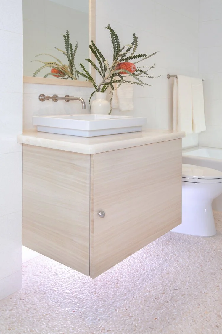 Photo by: Chas Metivier
This serene guest bathroom has a custom vanity cabinet and matching wood framed mirror that float above the cream colored pebble flooring.