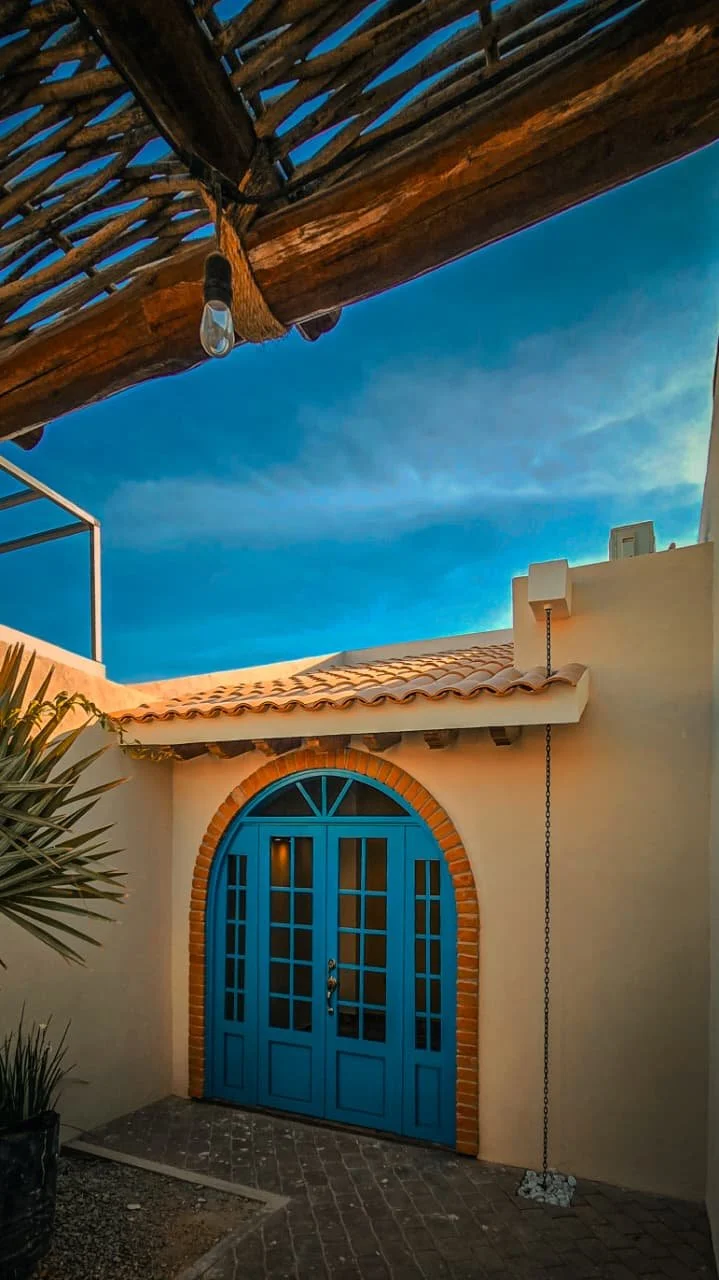 Puerta azul en una casa con detalles en ladrillo, techo de tejas y cielo despejado en el fondo.
