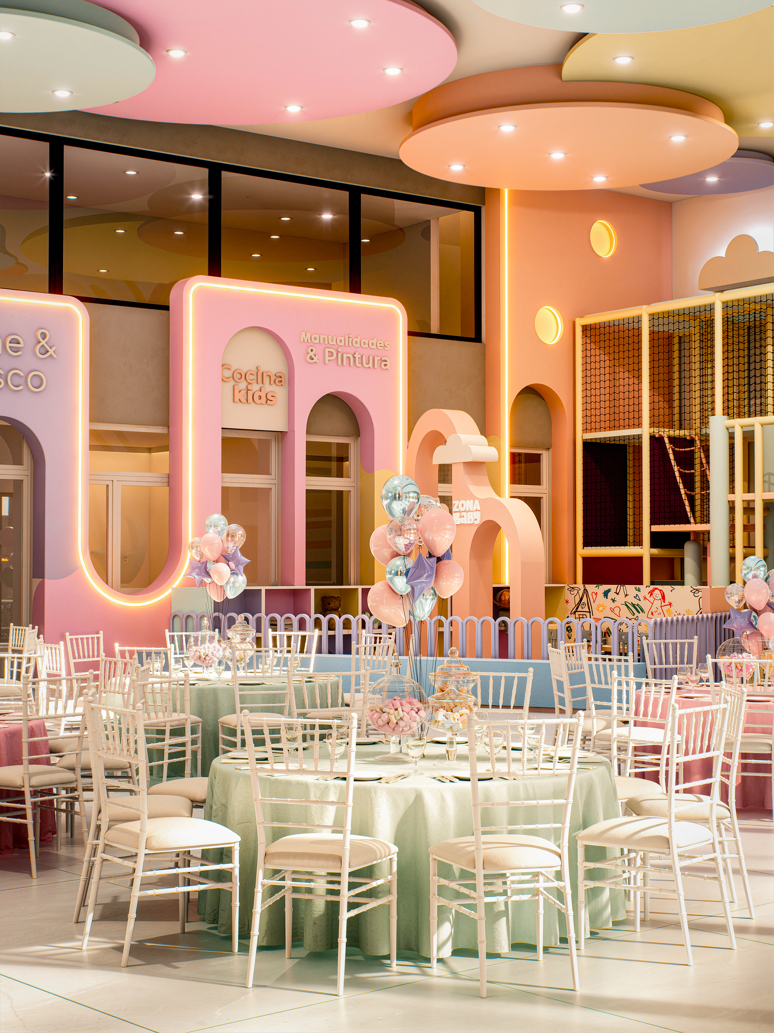 Área de fiesta decorada con mesas redondas, sillas blancas, globos rosas, lilas y celestes, y paredes en tonos pastel con cartel de nombres "Cocina kids" y "Manualidades & Pintura". Decoraciones en tonos rosa, lila y amarillo en ambiente infantil y f
