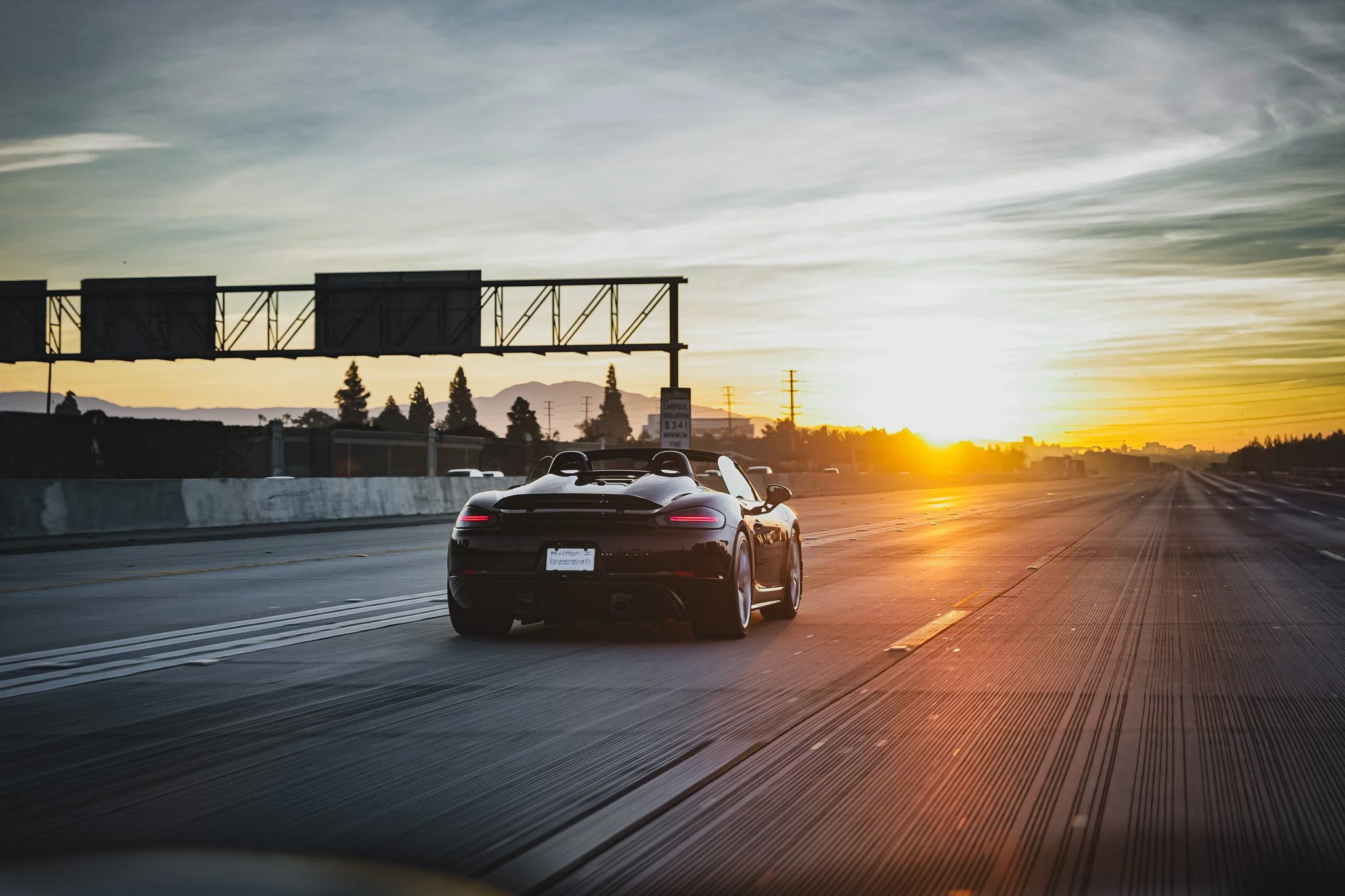 A black convertible sports car driving on a highway during sunset.