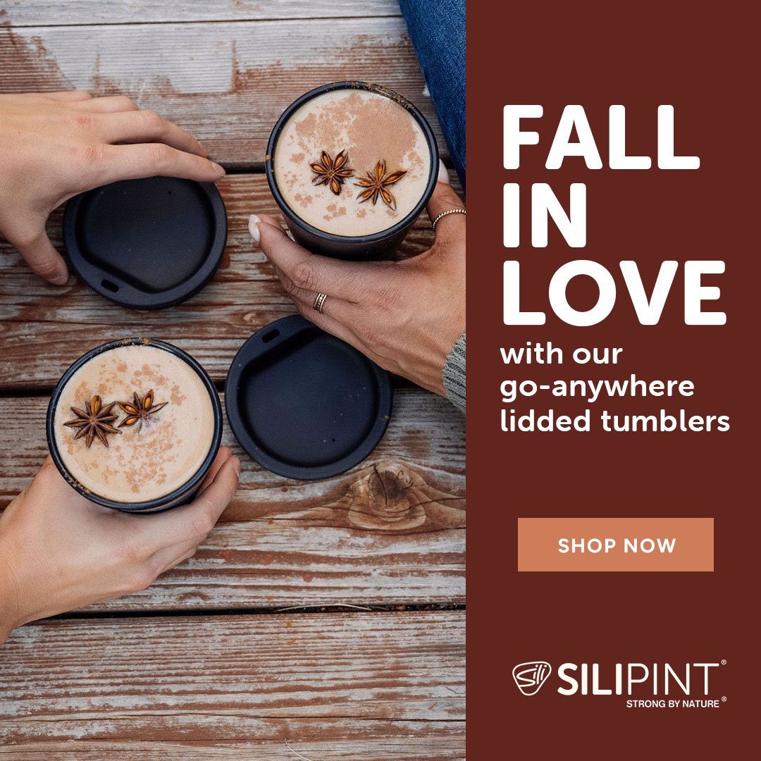 Two hands holding open lid of a black tumbler, revealing a beverage garnished with star anise spice on a wooden table.