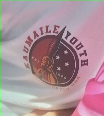 Close-up of a shirt with a logo saying 'Kaumaile Youth' and stars, in black, white, and pink colors.