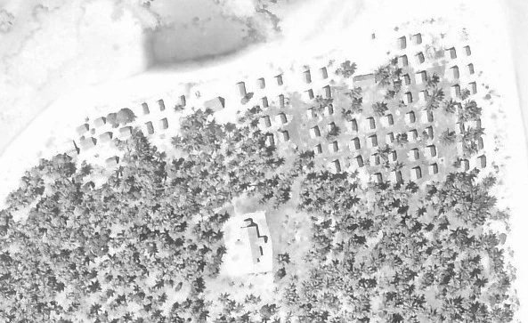 Black and white aerial view of E. tip of Lakena islet showing trees, church, and village thatched houses near the lagoon.