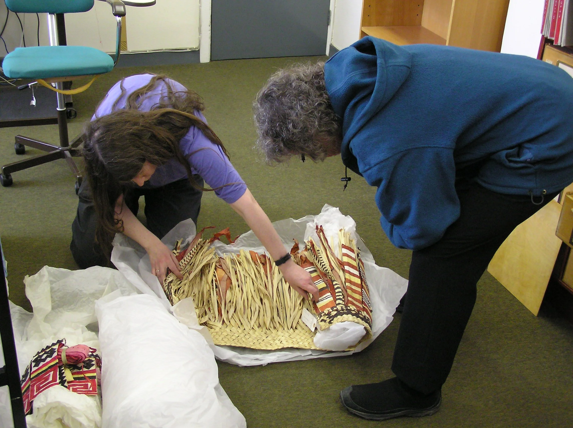 Two people handling a woven basket full of shredded paper and textiles.