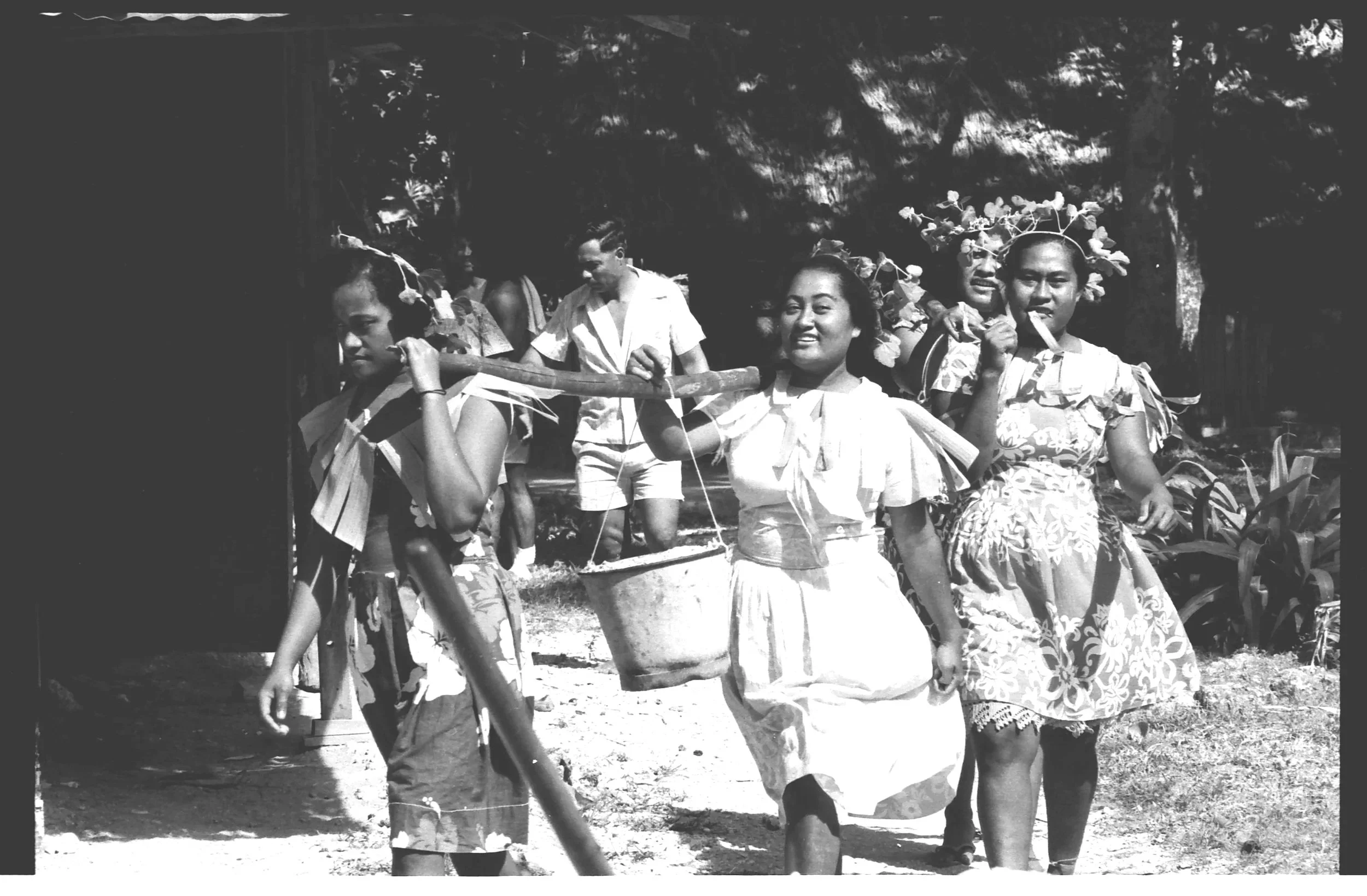 Women and children dressed in traditional attire carrying baskets of sand during communal work on a new island cistern.