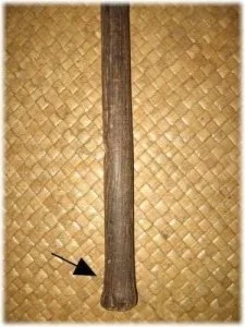 Kaumaile wooden spear with arrow showing to a section near the bottom, placed on a woven mat background.