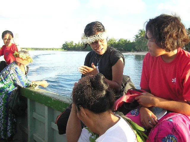 Group of young people on a work boat leaving Nanumea's lagoon - some wearing flower crowns, engaging in conversation.