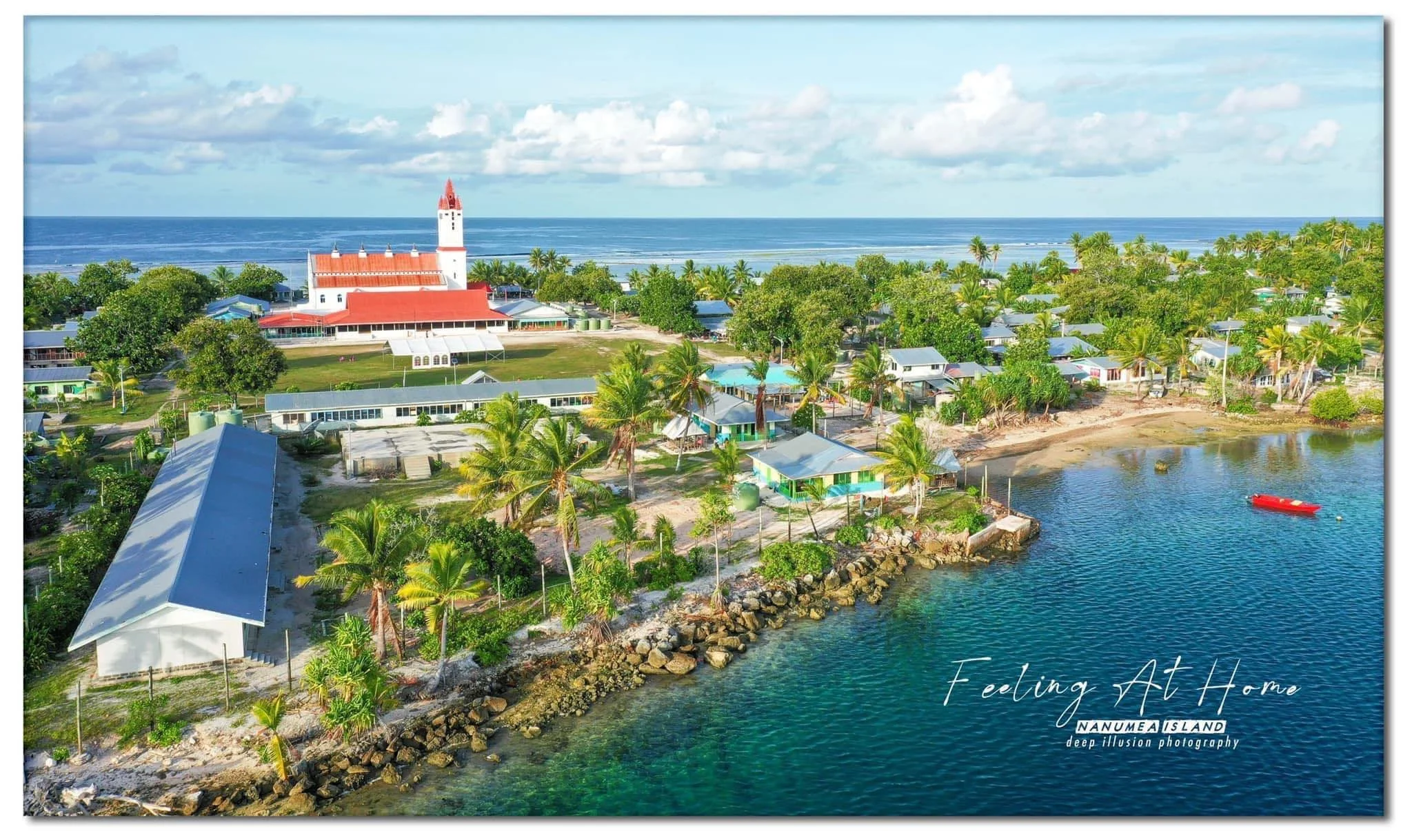 Aerial view of Nanumea's main village with the church, colorful houses, palm trees, a lagoon shoreline and the ocean in the background.