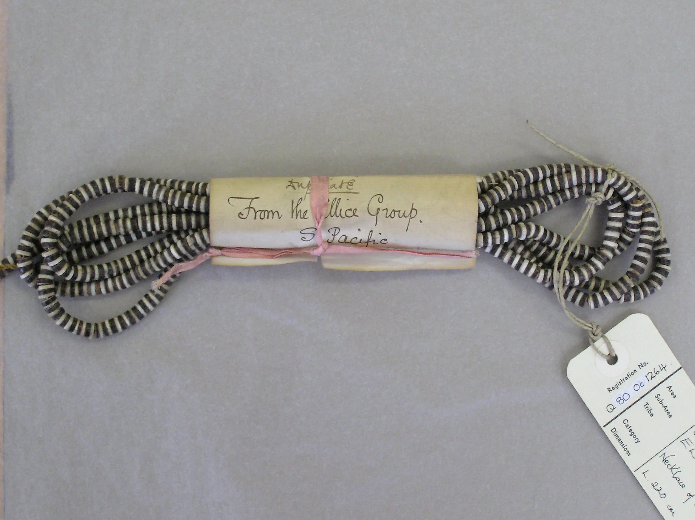 A bundle of black and white beads from the Ellice Islands in the 19th C. Attached to the bundle is a white tag with registration and catalog information.