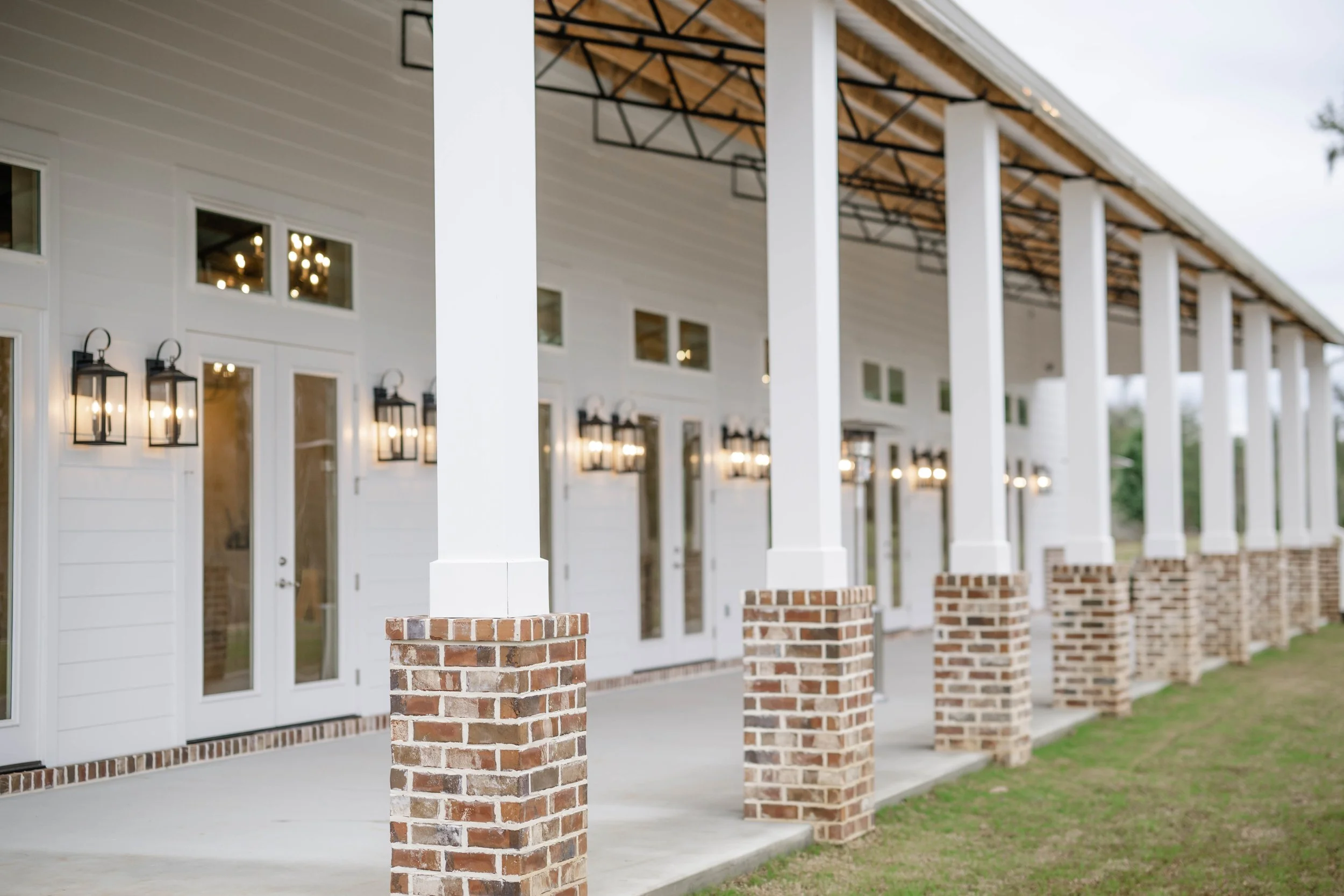 Exterior of Willow Point Venue's building with white pillars and brick bases, large windows, and hanging lantern-style lights.