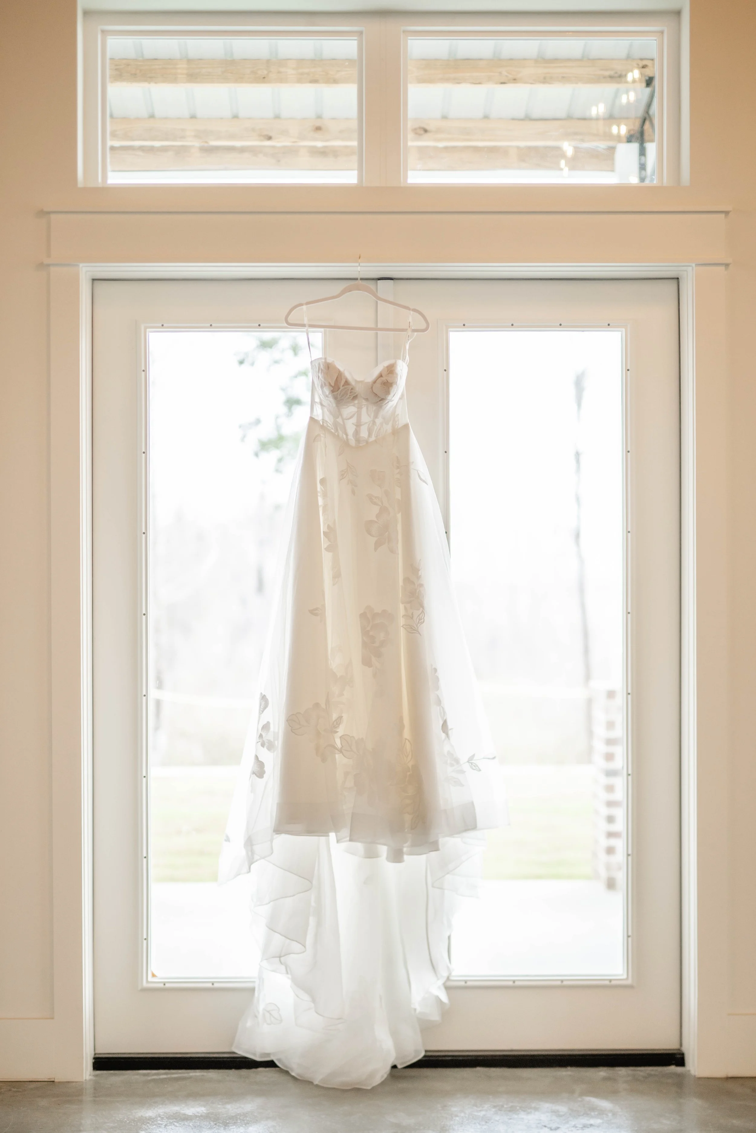 Wedding dress hanging on a door with sheer fabric and floral details at Willow Point Venue.