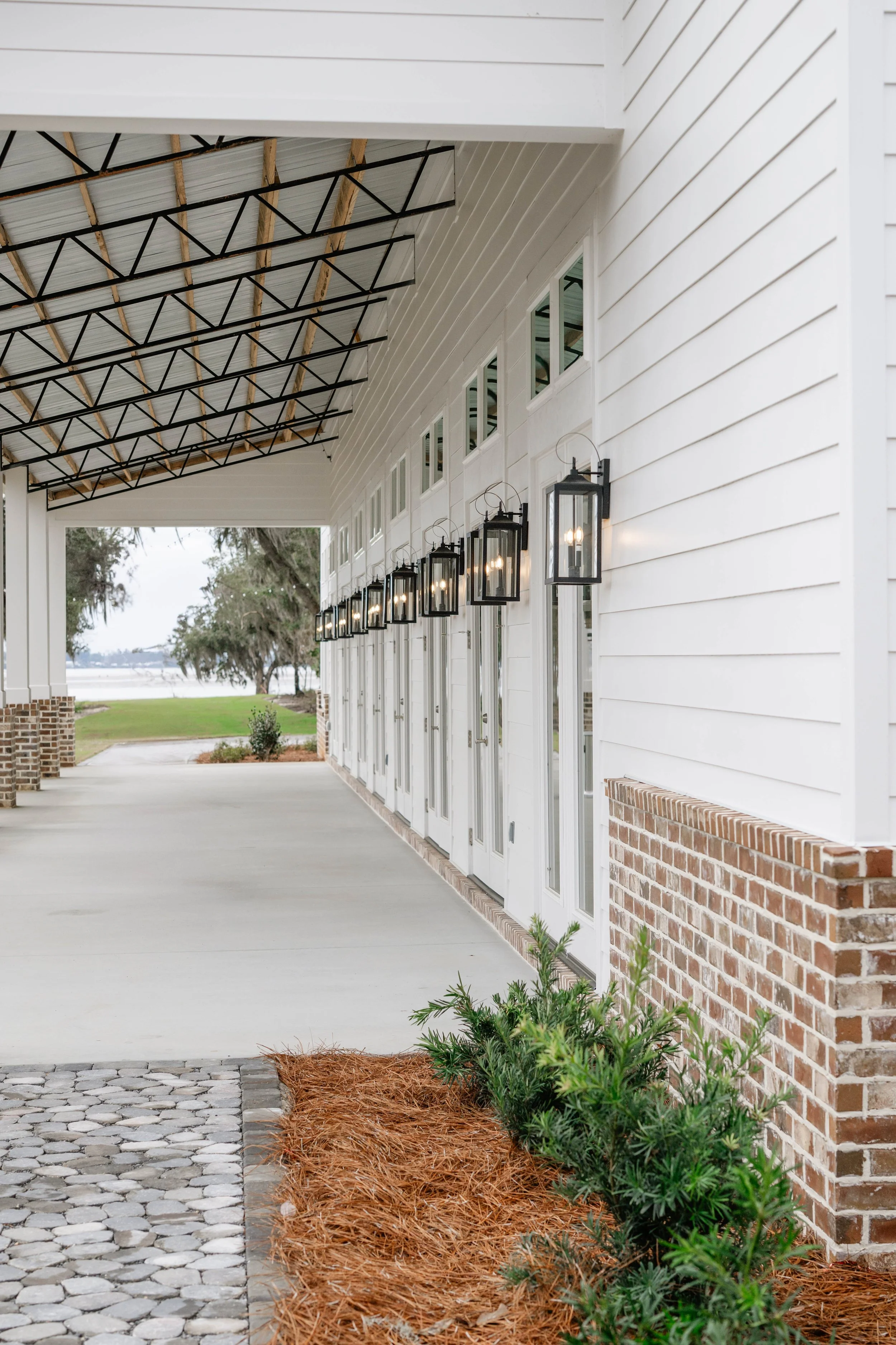 Outdoor walkway with glass doors, brick accents, black metal lanterns, and a sloped roof at Willow Point Venue.