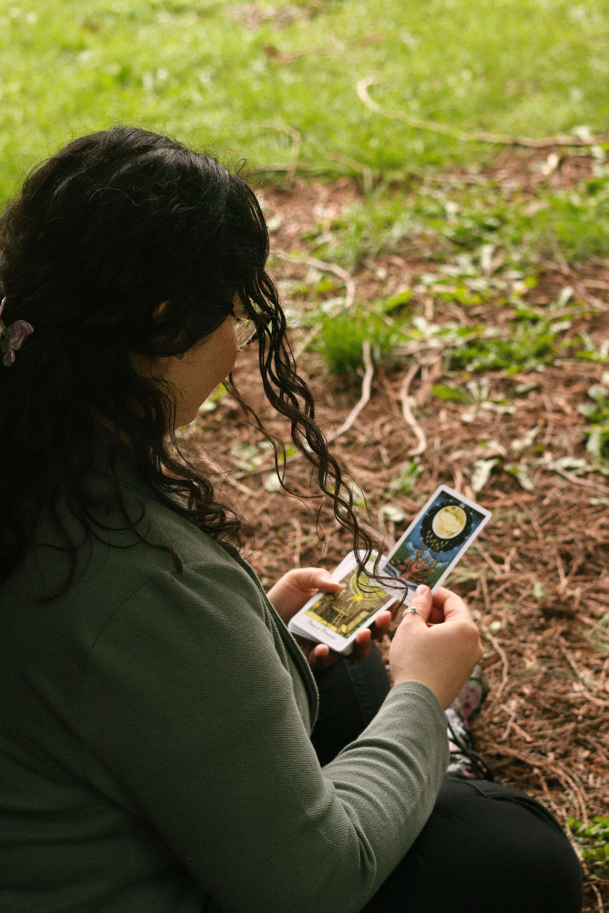 Person holding tarot cards outdoors, with one card of a skeleton labeled "Death" and a deck with celestial and zodiac symbols.