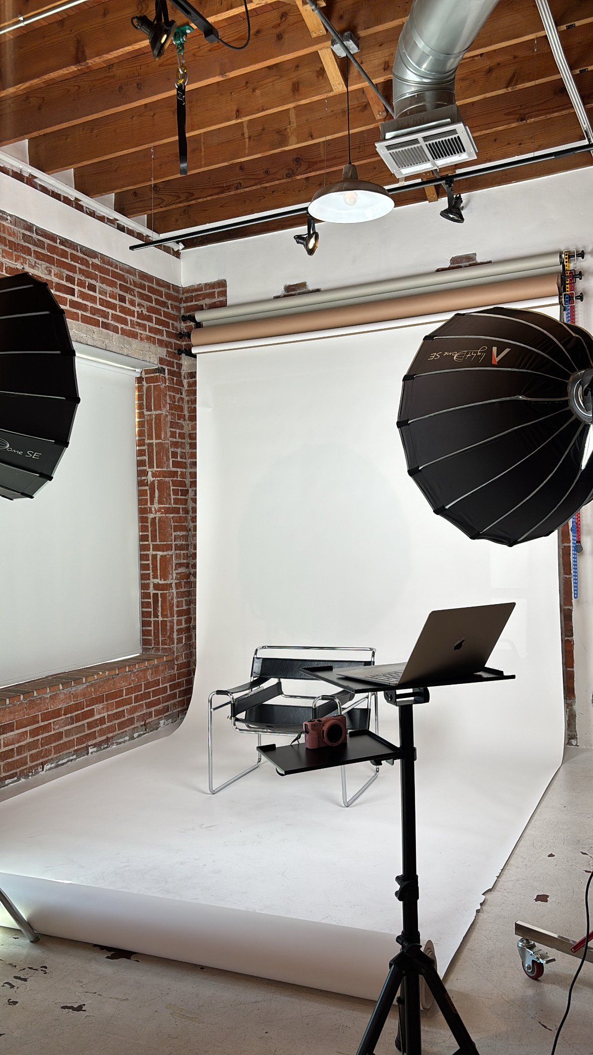A photography studio set up with a white backdrop and black chair.
