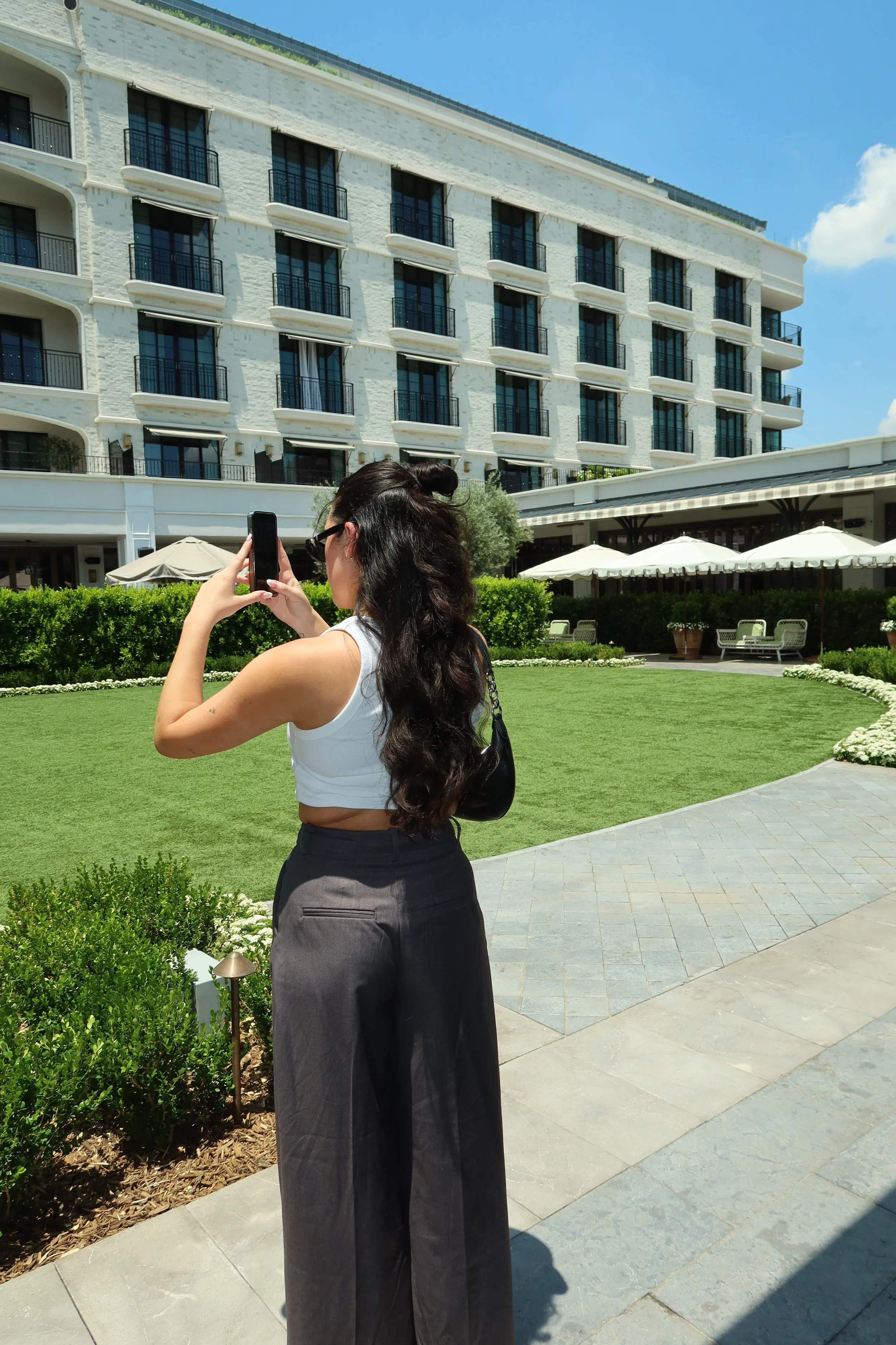 Woman with dark hair taking a photo in front of a hotel.