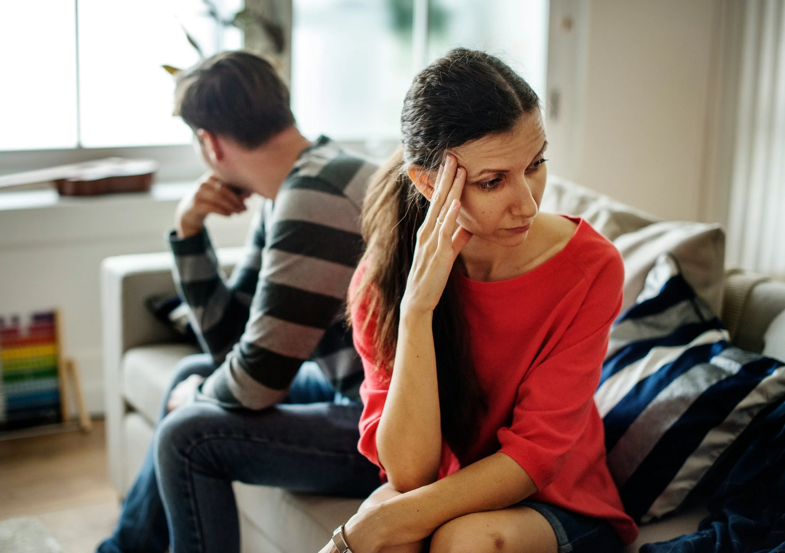 A couple sitting apart on a couch during conflict, illustrating the emotional strain families in transition face and the need for trauma-informed family support during high-conflict transitions.
