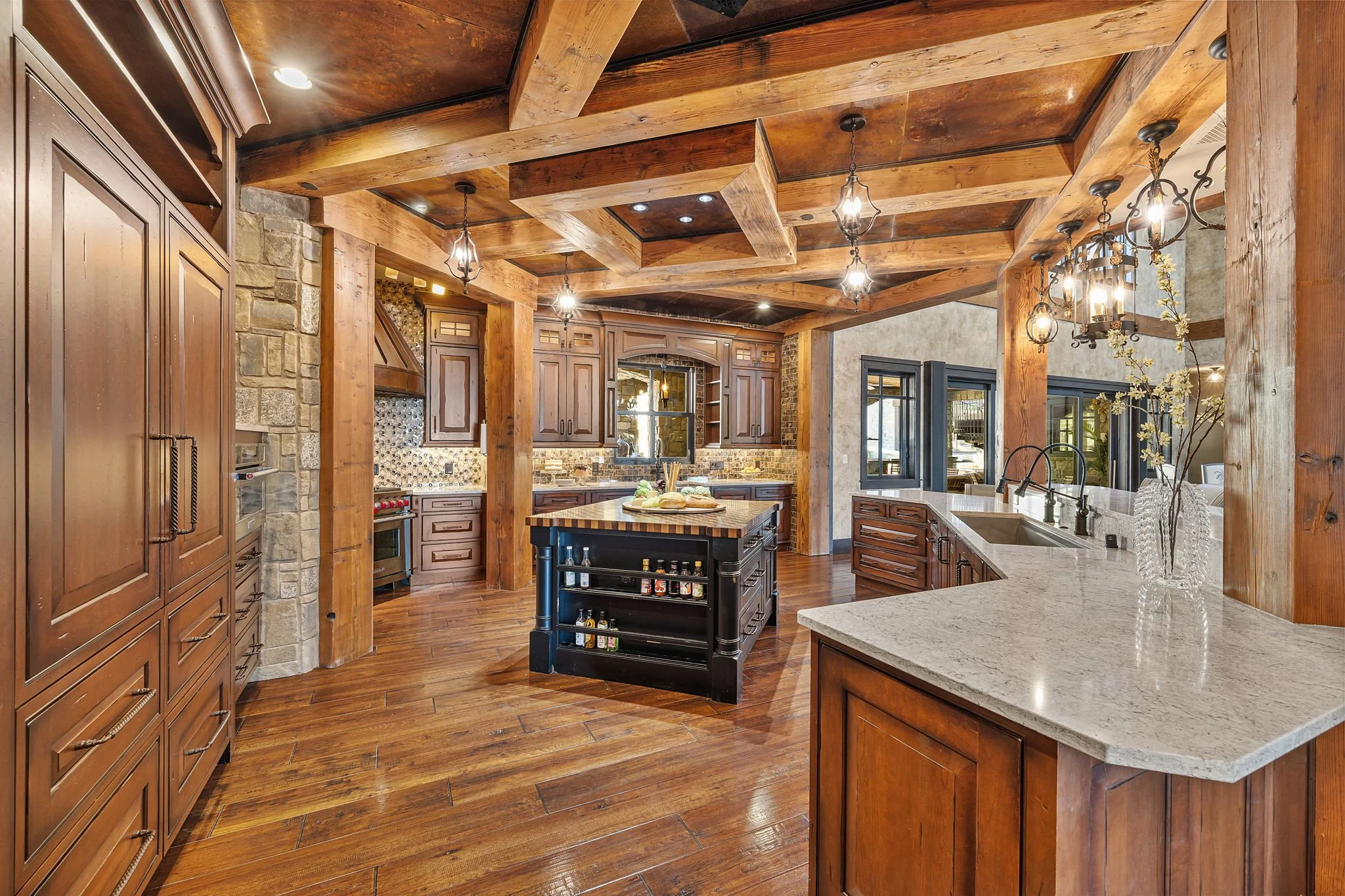 Rustic kitchen with wooden cabinets, hardwood floors, stone accent wall, granite countertops, and chandelier lighting.
