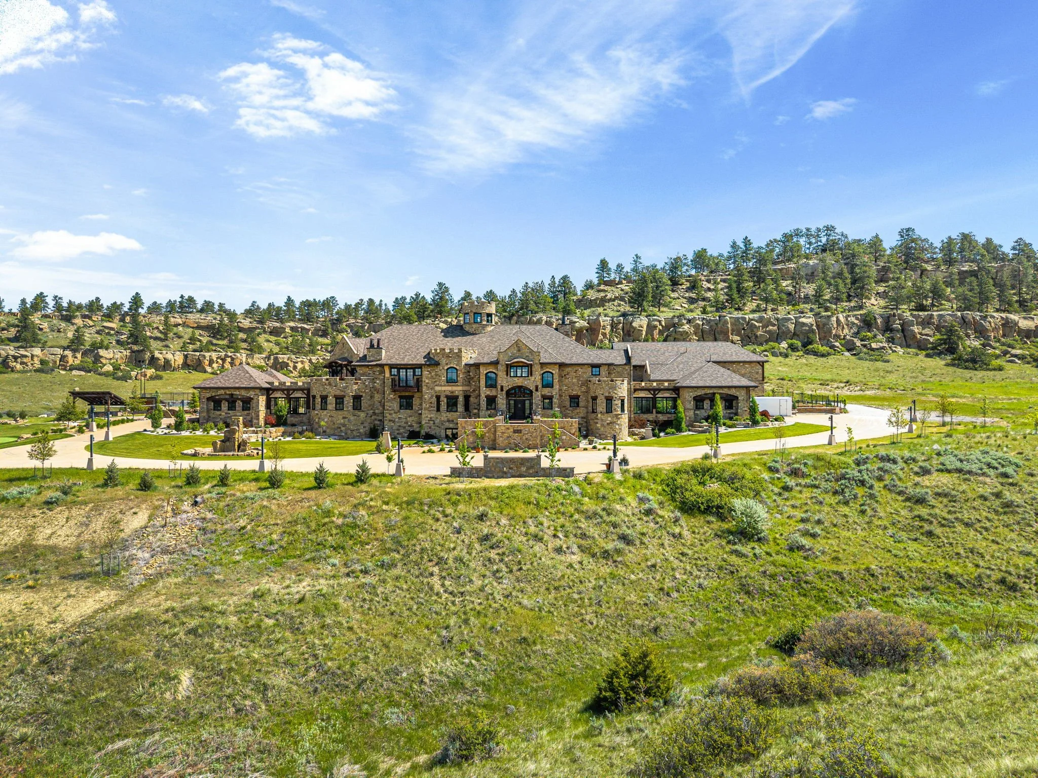 Large stone mansion on a grassy hill under a blue sky with scattered clouds.