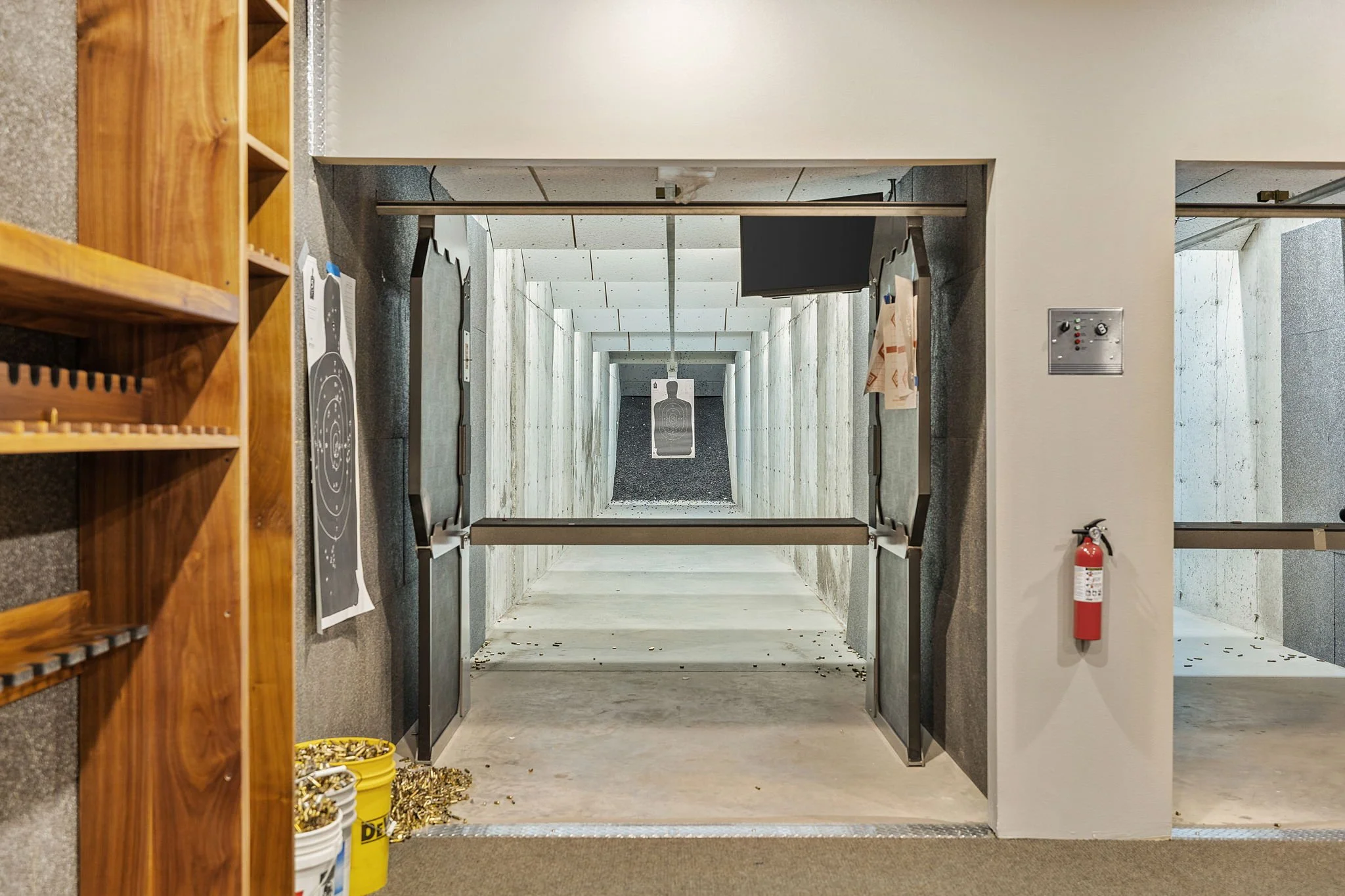 An indoor shooting range with a target at the far end and bullet shells scattered on the floor, seen through an open door.