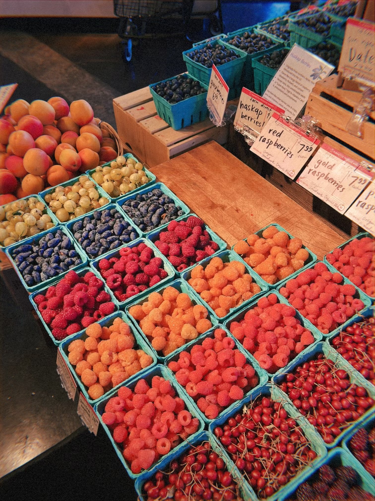 Display of fresh berries, including cape gooseberries, blueberries, raspberries, golden raspberries, and cherries in baskets at a market stand.