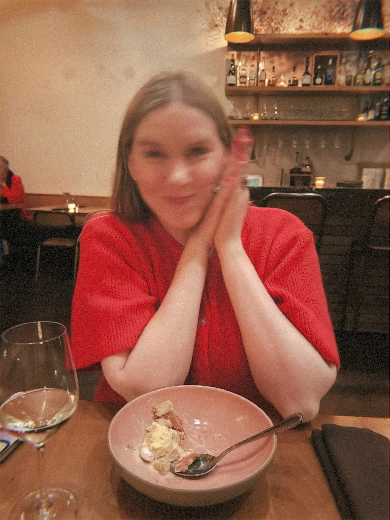 Heather Leith, a freelance copywriter for weddings and events, is in a red sweater sitting in a cozy restaurant with an excited look on her face. On the table is a pink plate of partially eaten food, a spoon, and a glass of water.