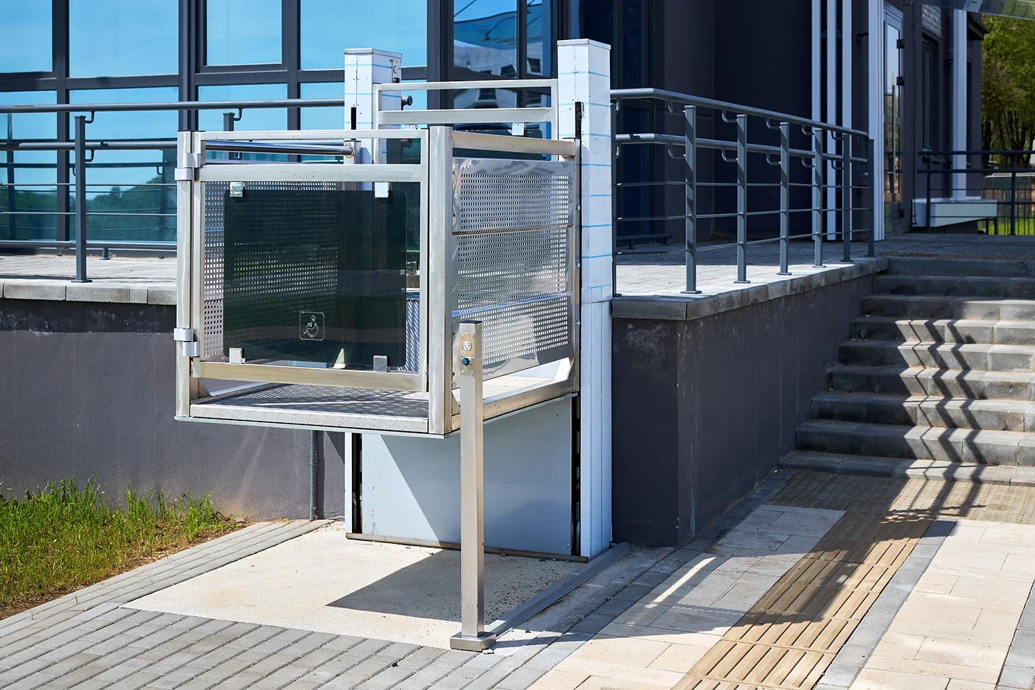 Outdoor accessibility lift for wheelchair users beside a flight of stairs with a metal railing.