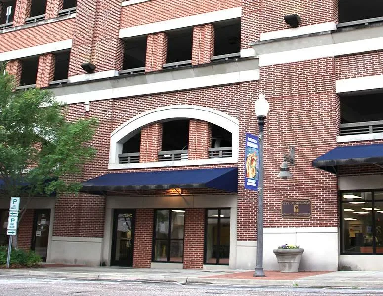 Brick building with arched windows, blue awnings, green tree, lamppost, and city of medina sign.