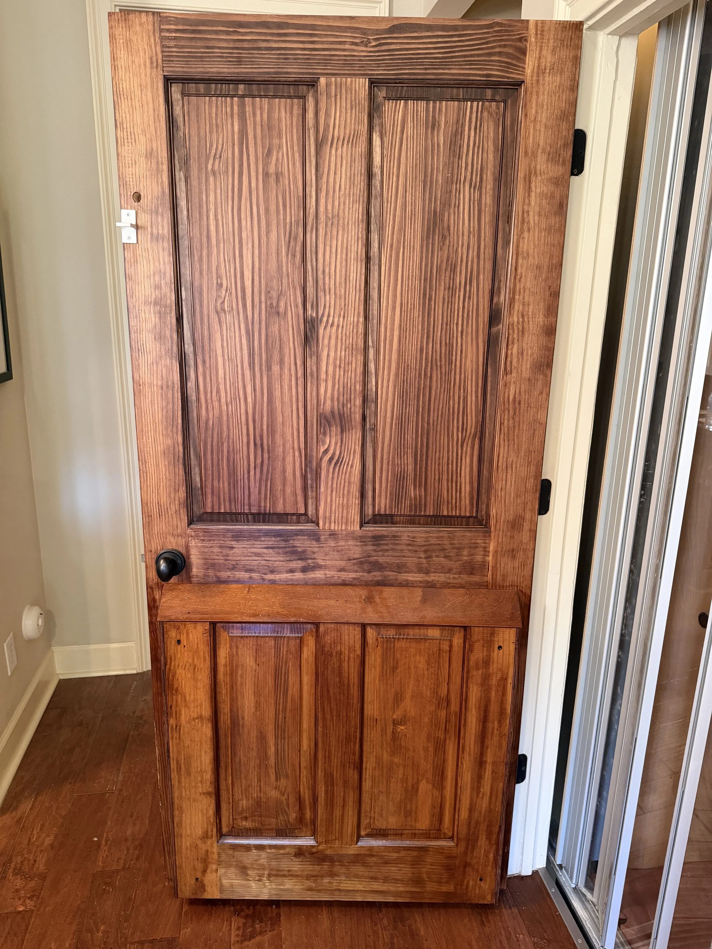 A wooden cabinet with two upper doors and two lower doors, placed indoors near a wall and beside a metal door frame.