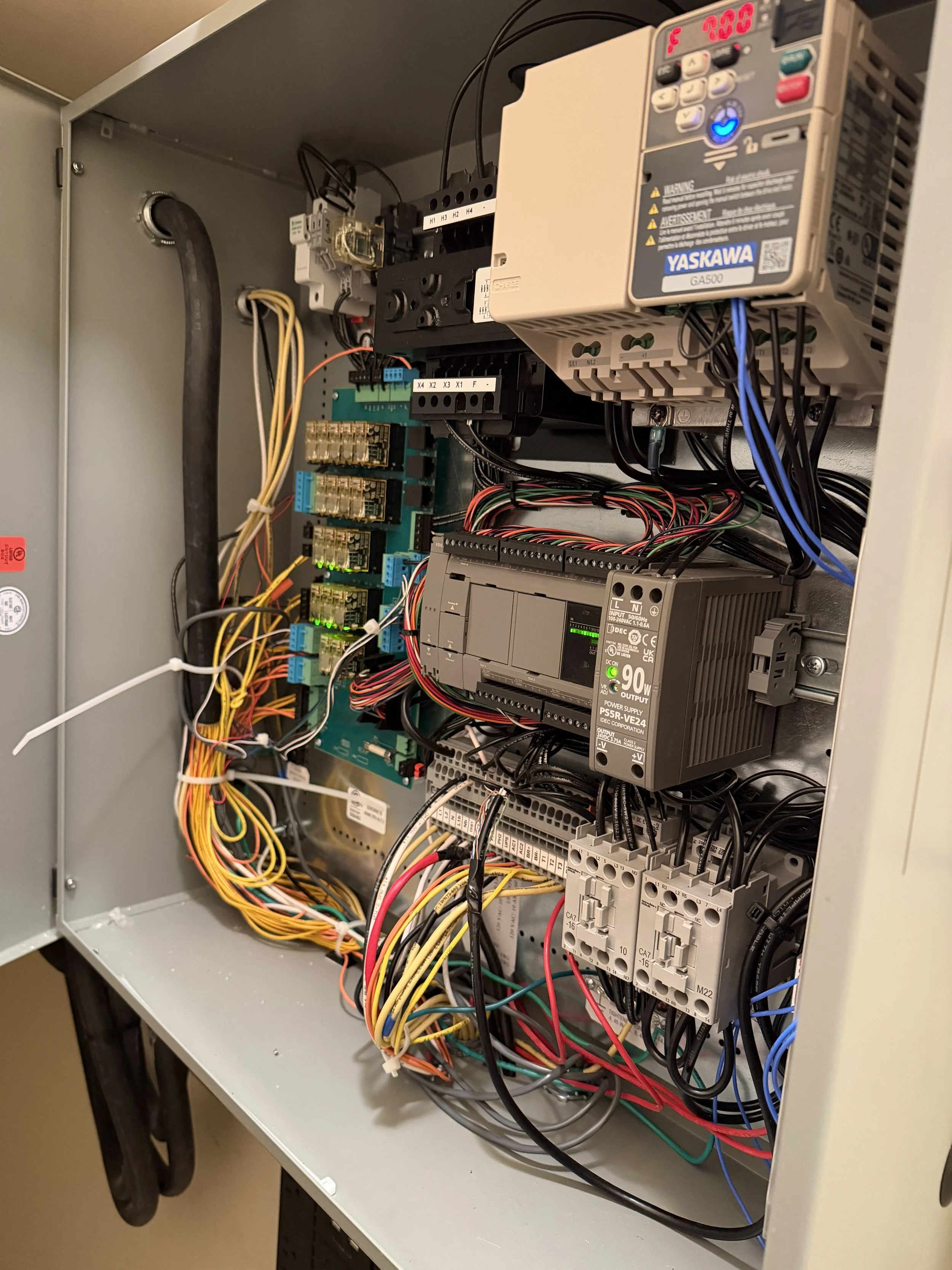 An open electrical control panel with various wires, relays, circuit boards, and a power supply unit.