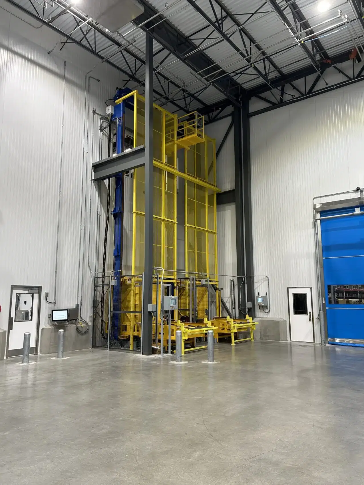 Industrial freight elevator inside a warehouse with safety barriers, control panels, and metallic walls and ceiling.