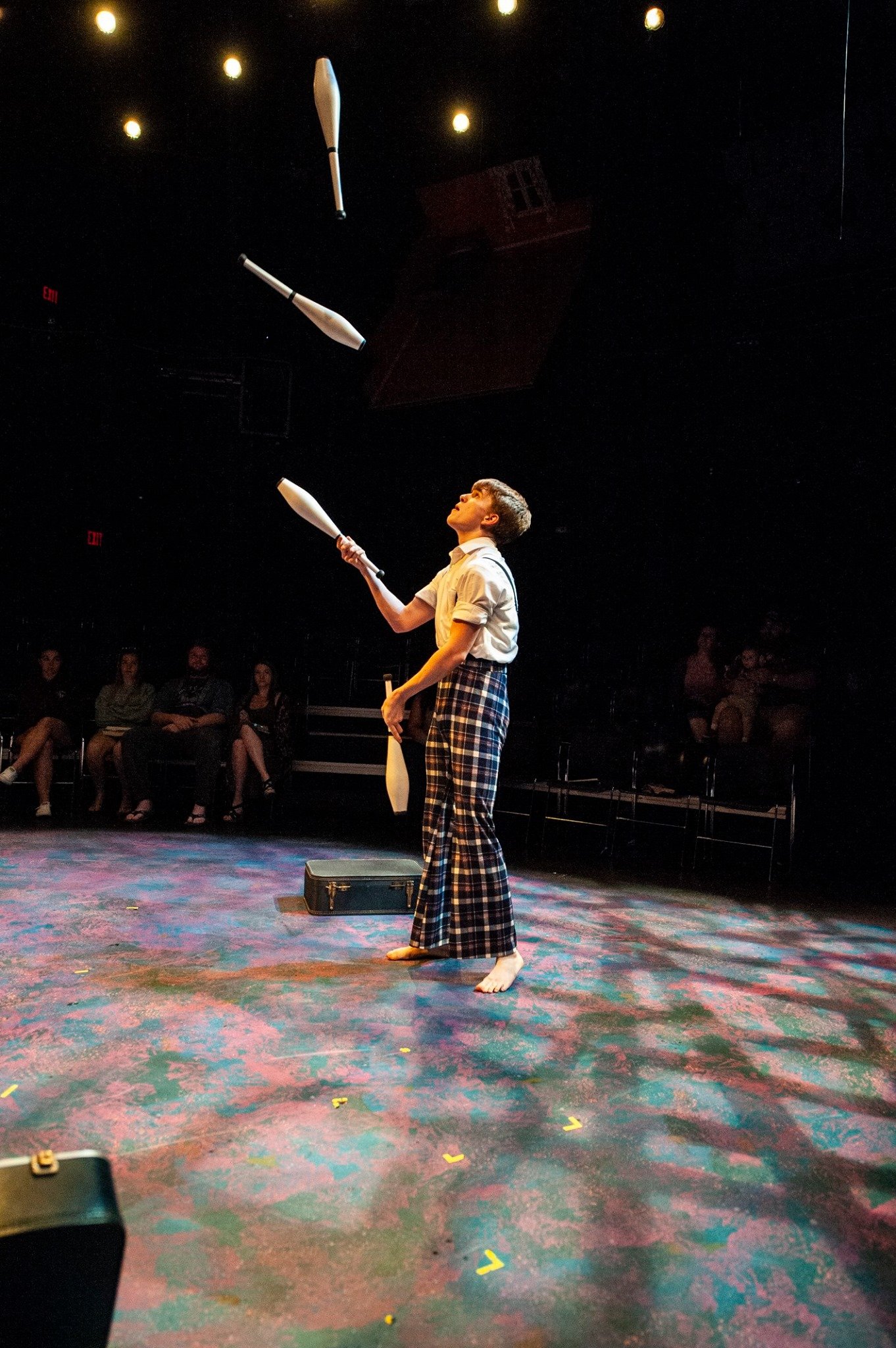 Performer juggling clubs on a colorful stage in a theater. Noah Dach creative director.